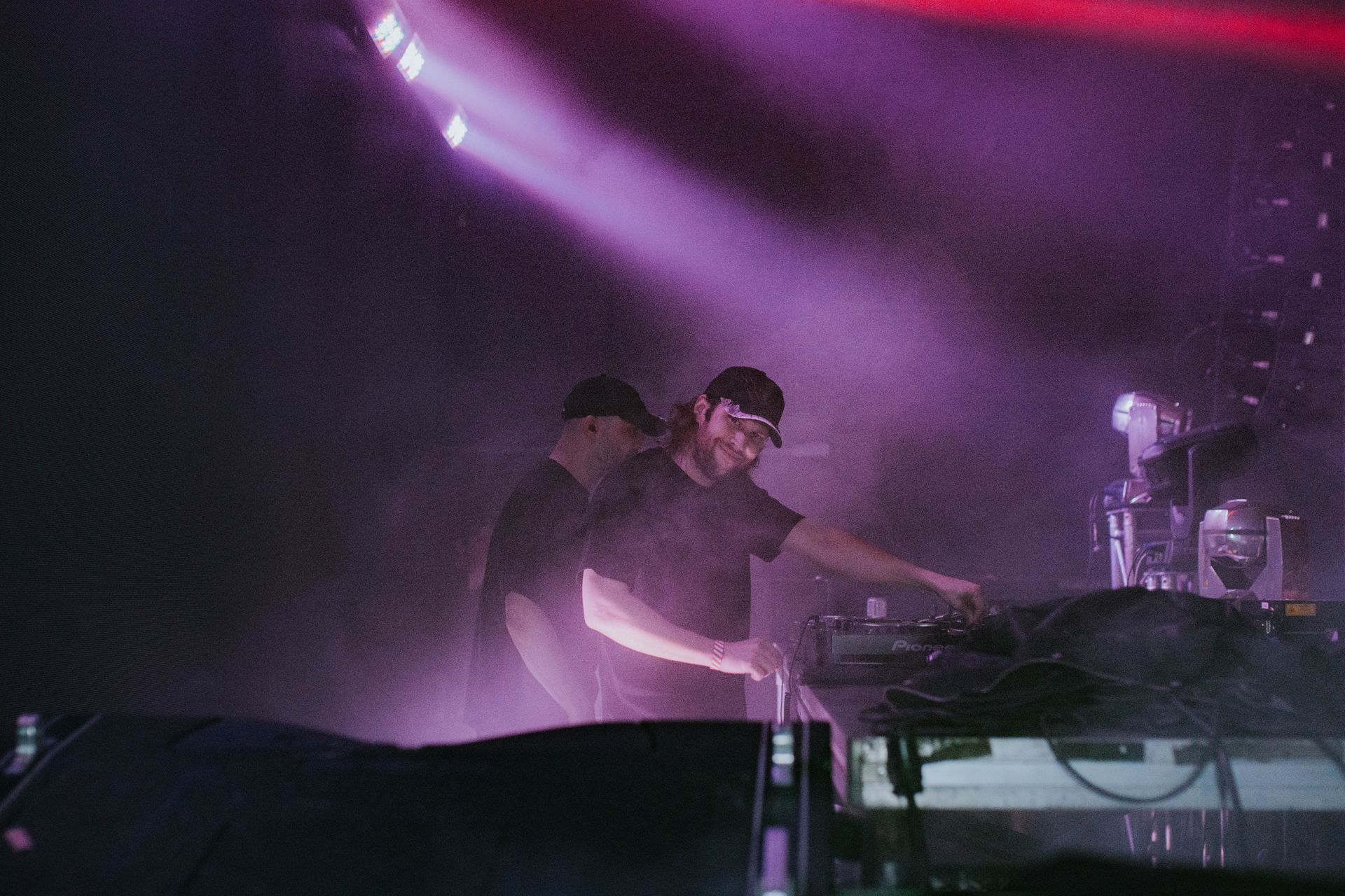 Two men are playing music on a stage with purple lights behind them.