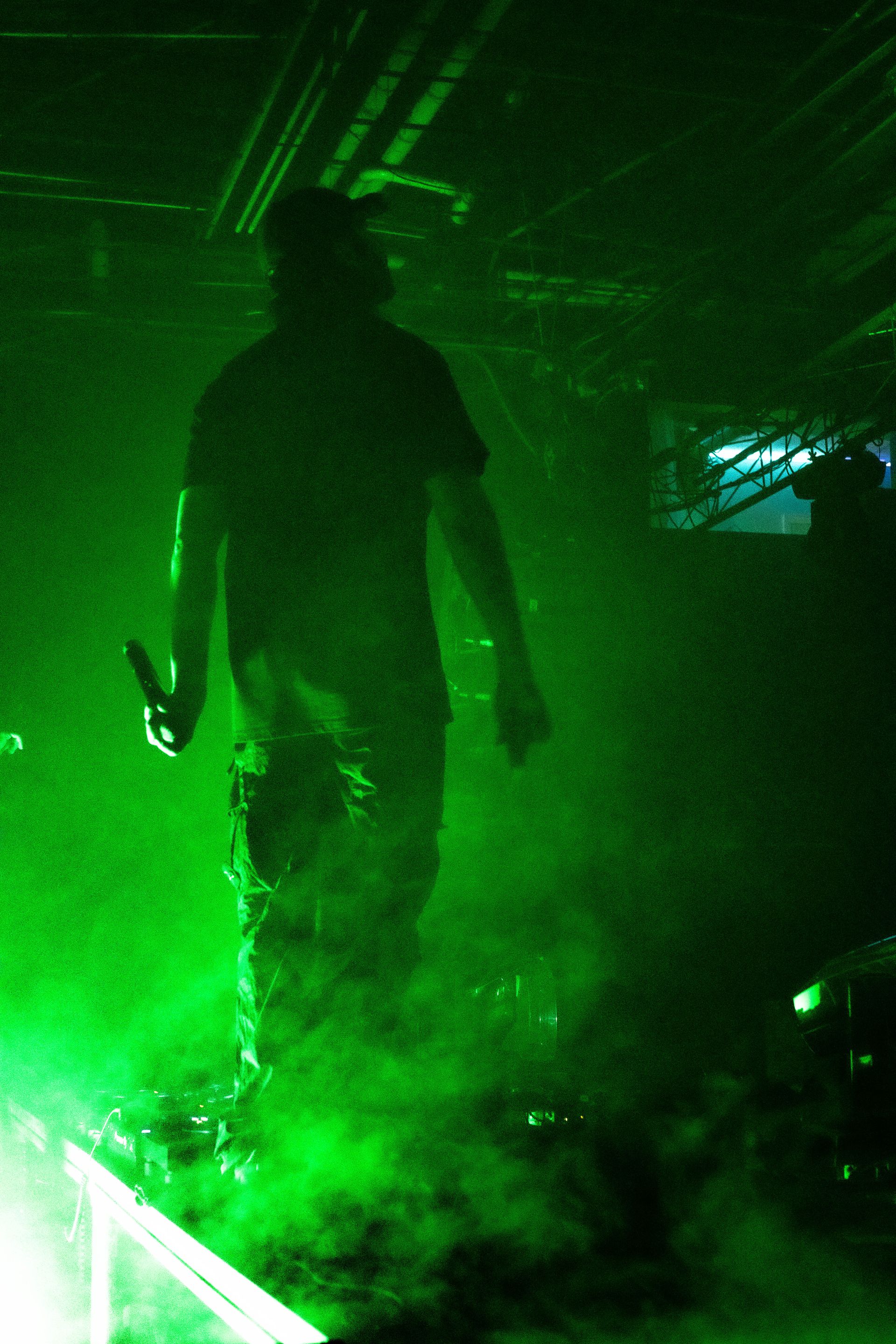 A man is walking through a green foggy room holding a microphone.