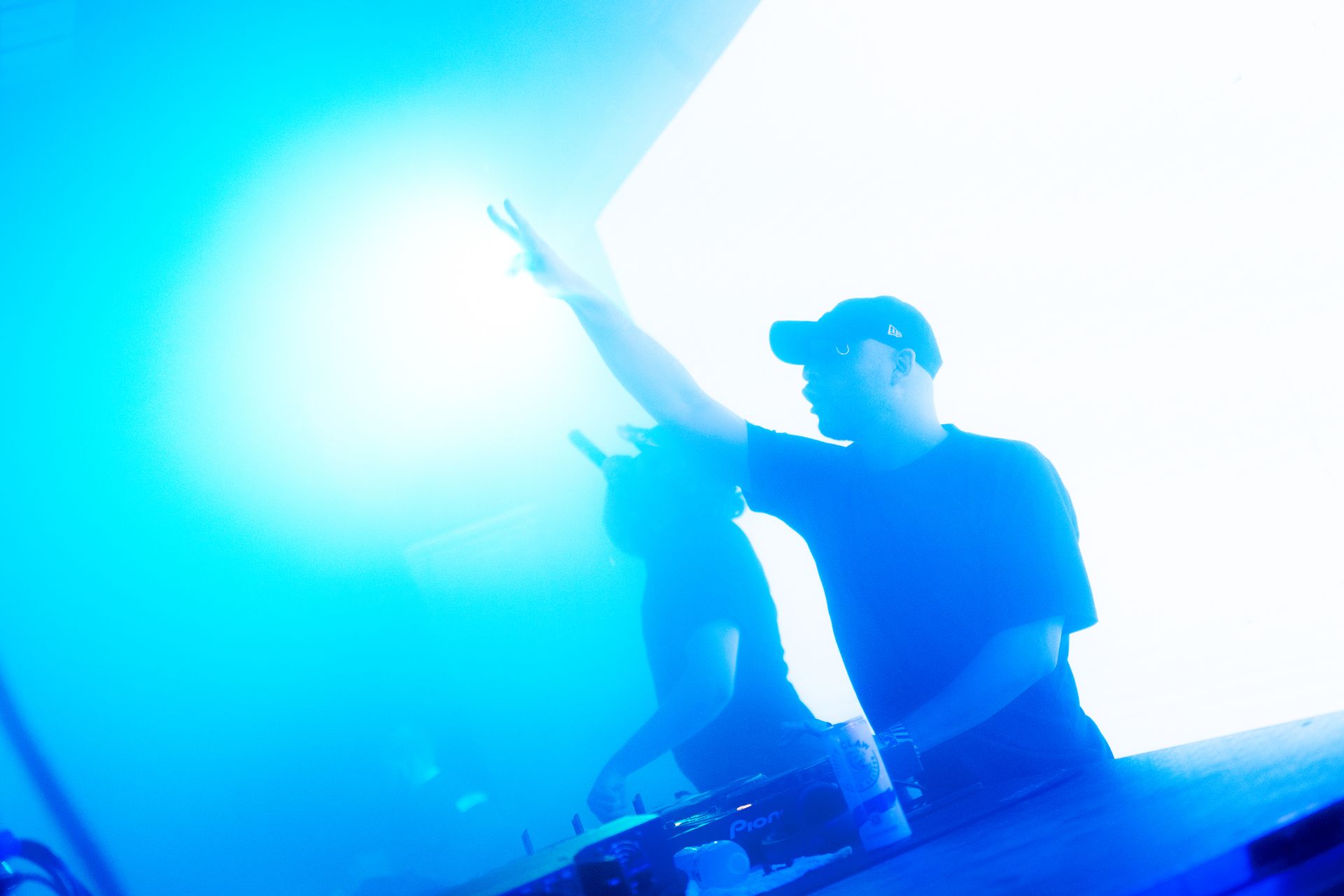 A man in a hat is playing a dj set in front of a blue light.