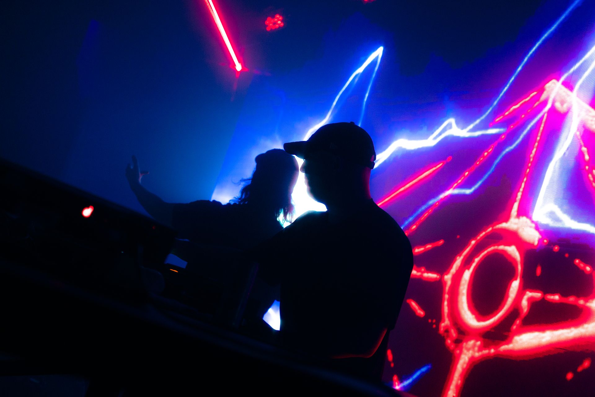 A man and a woman are standing in front of a colorful light show in a dark room.