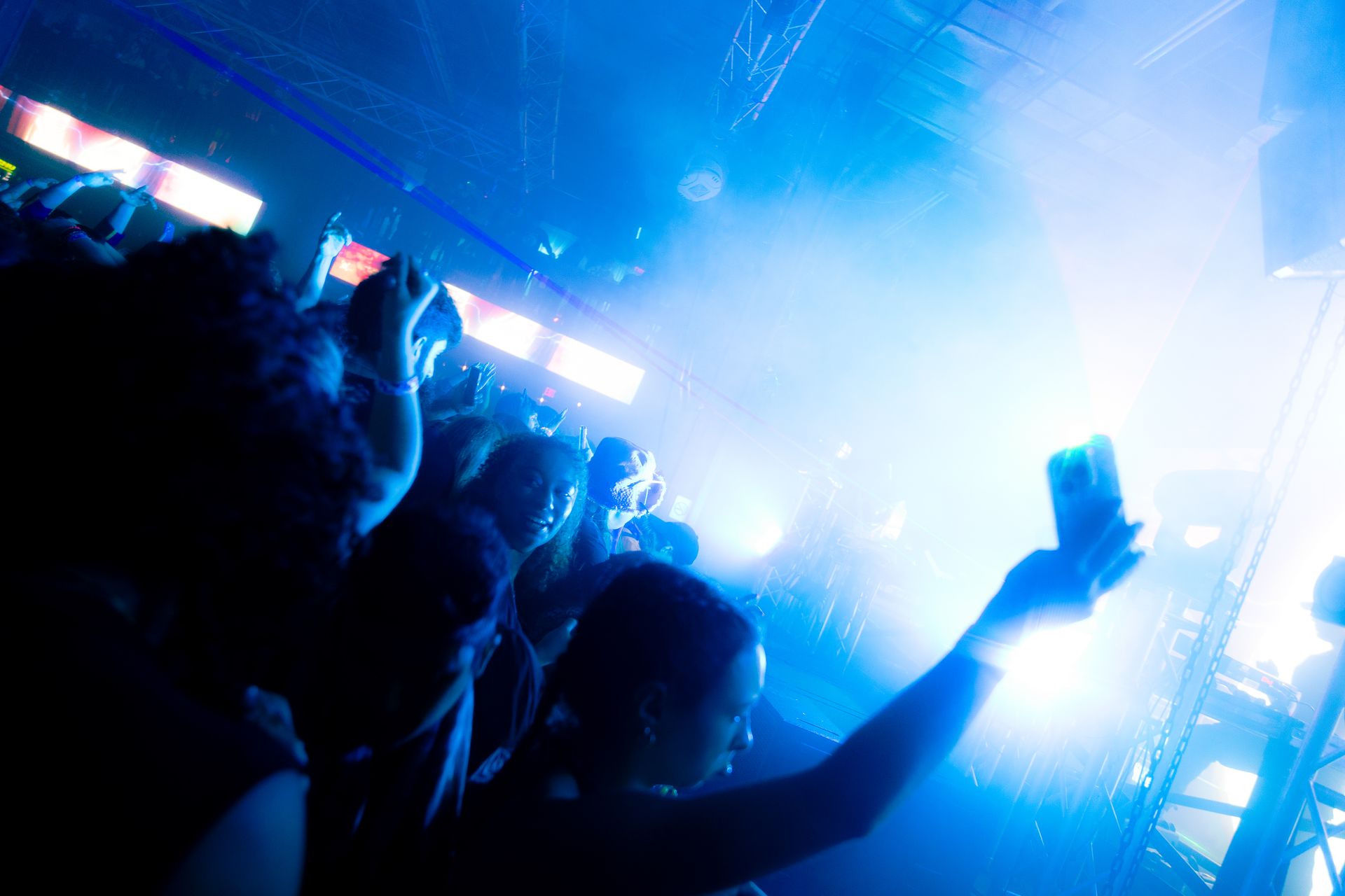 A crowd of people at a concert with their arms in the air.
