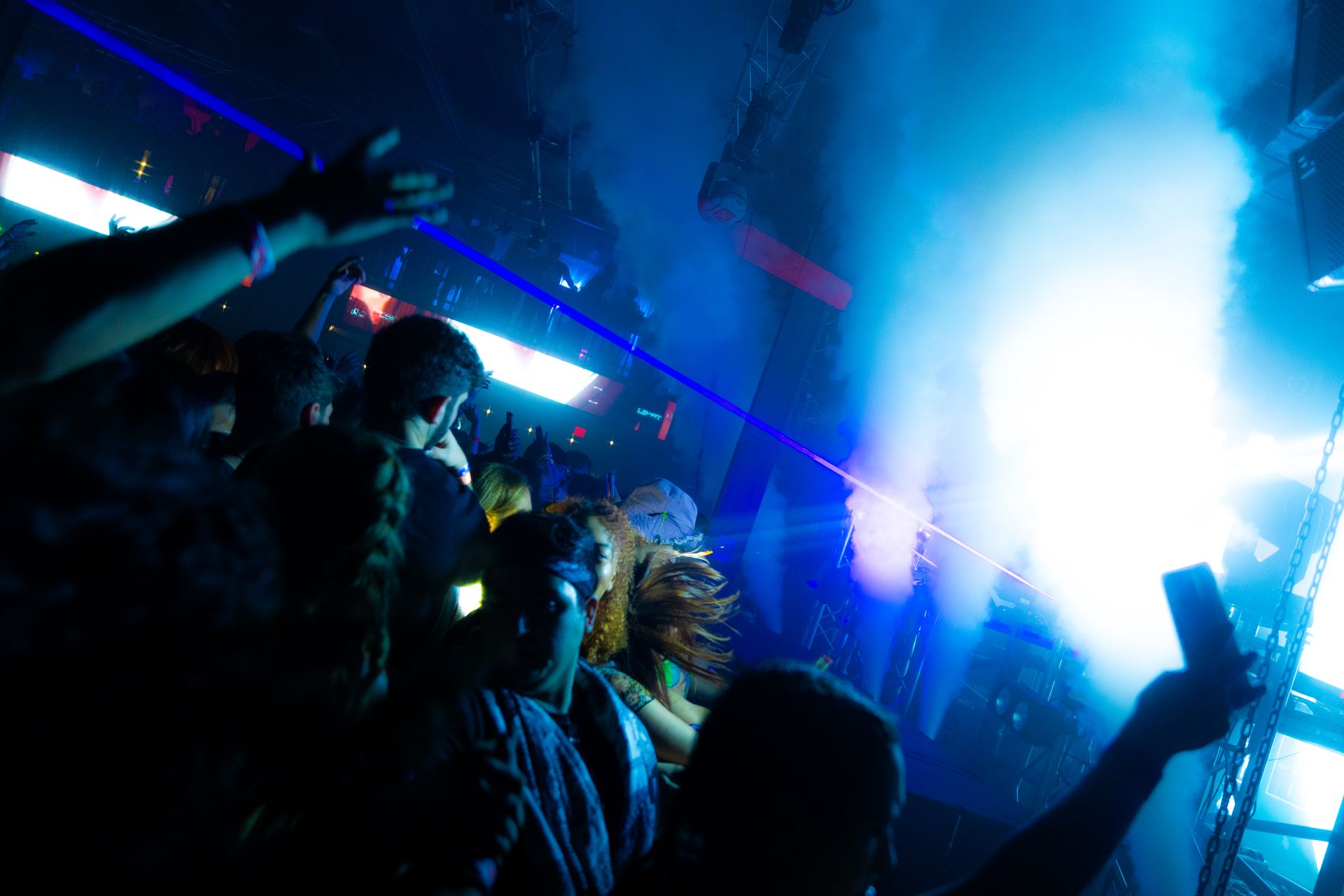 A crowd of people are standing in a dark room with smoke coming out of the ceiling.