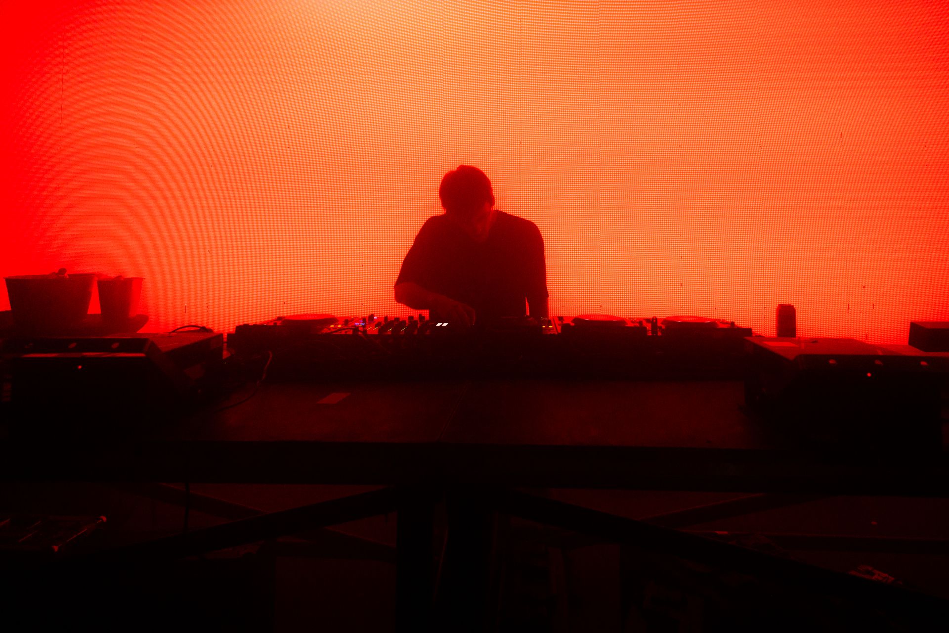 A silhouette of a dj playing music in front of a red background.