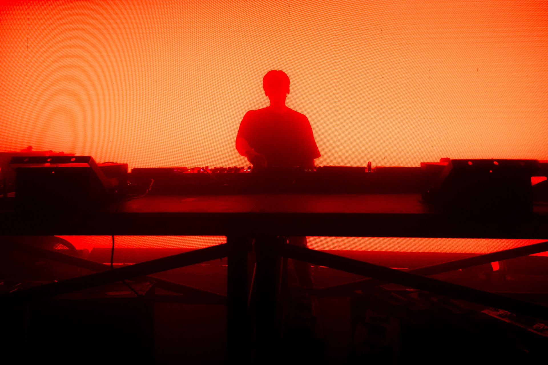 A silhouette of a man playing a dj set in front of a red background.