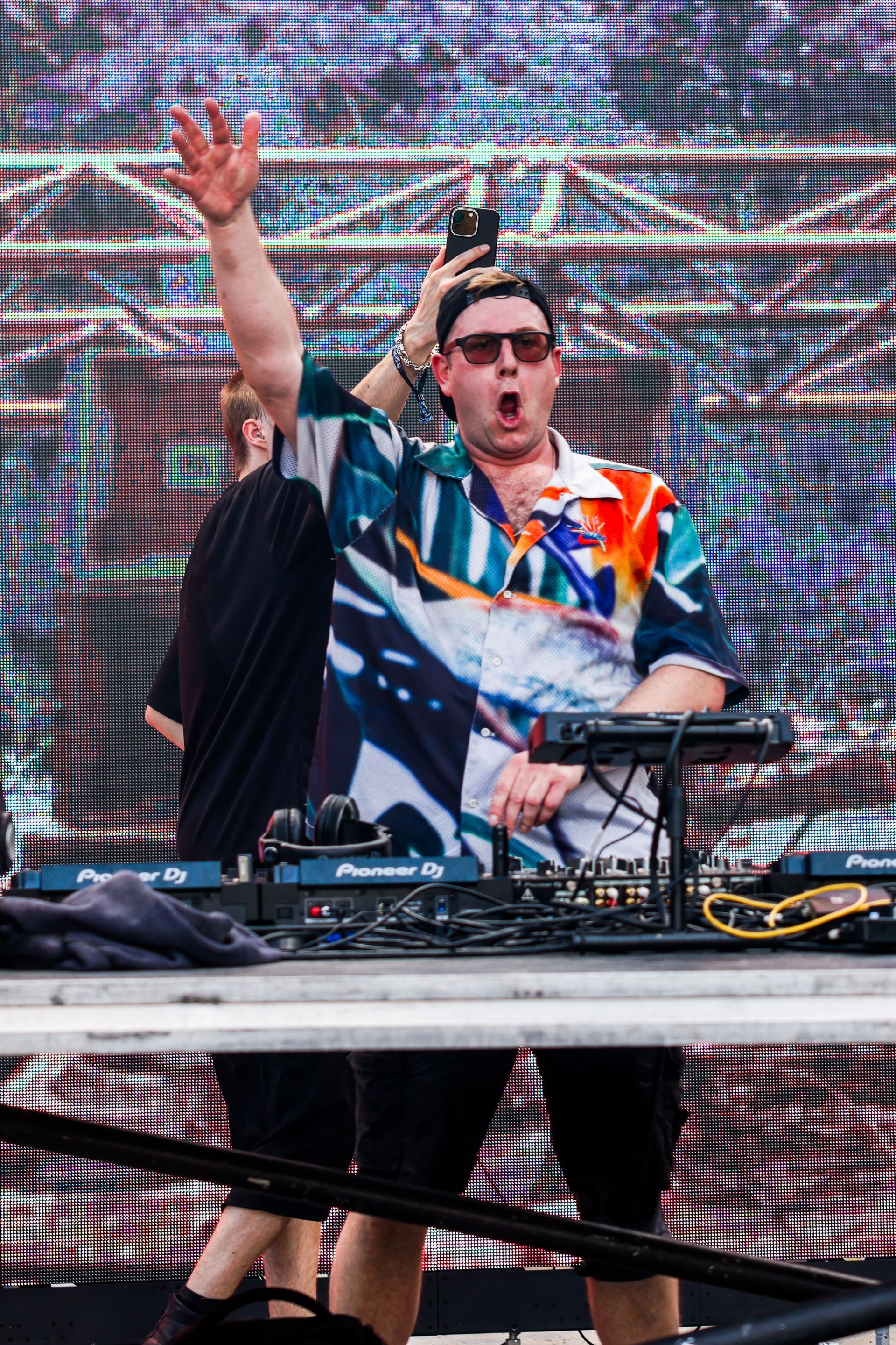 A man is standing in front of a large screen playing a dj set.
