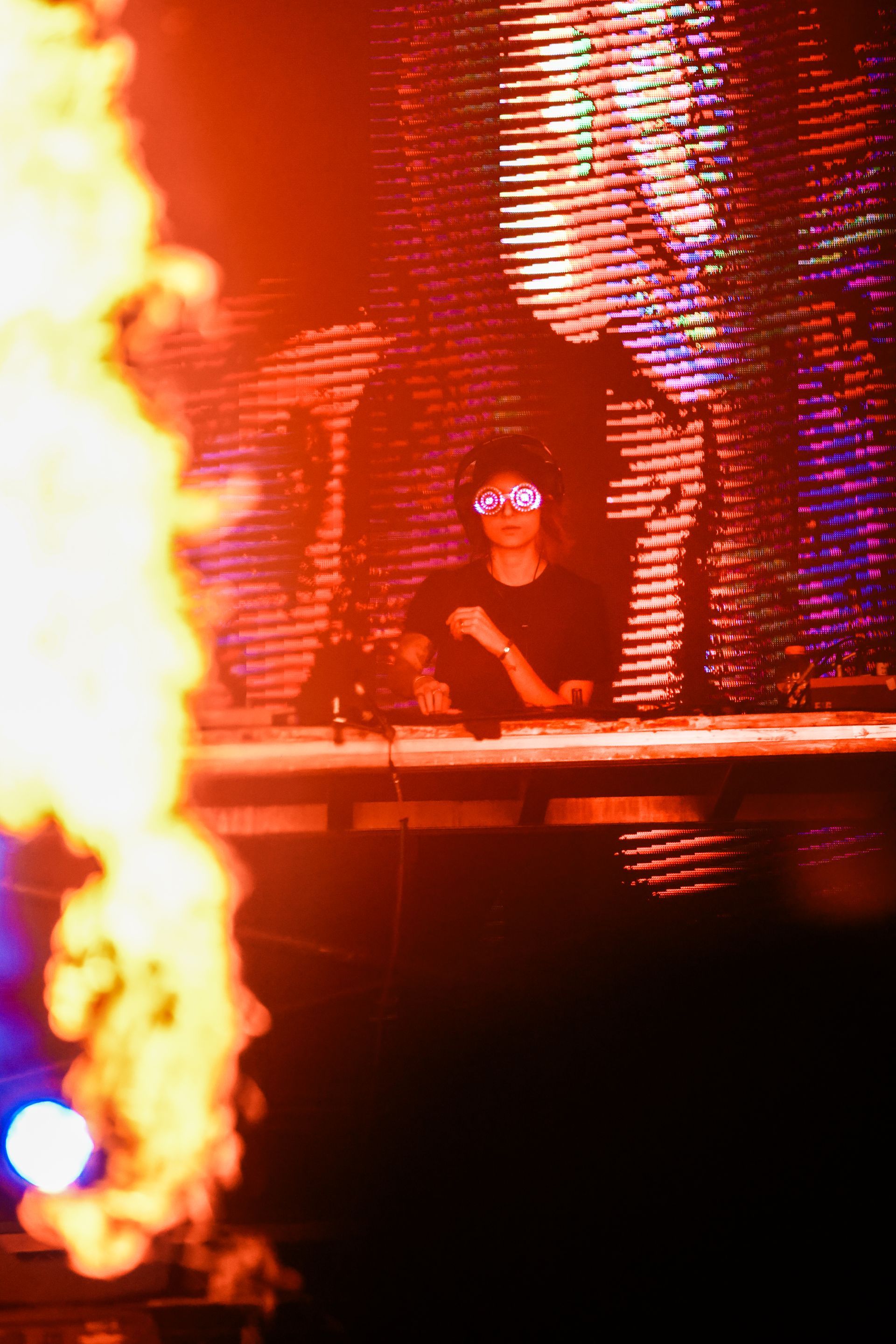 A dj is playing music on a stage in front of a large screen with flames coming out of it.