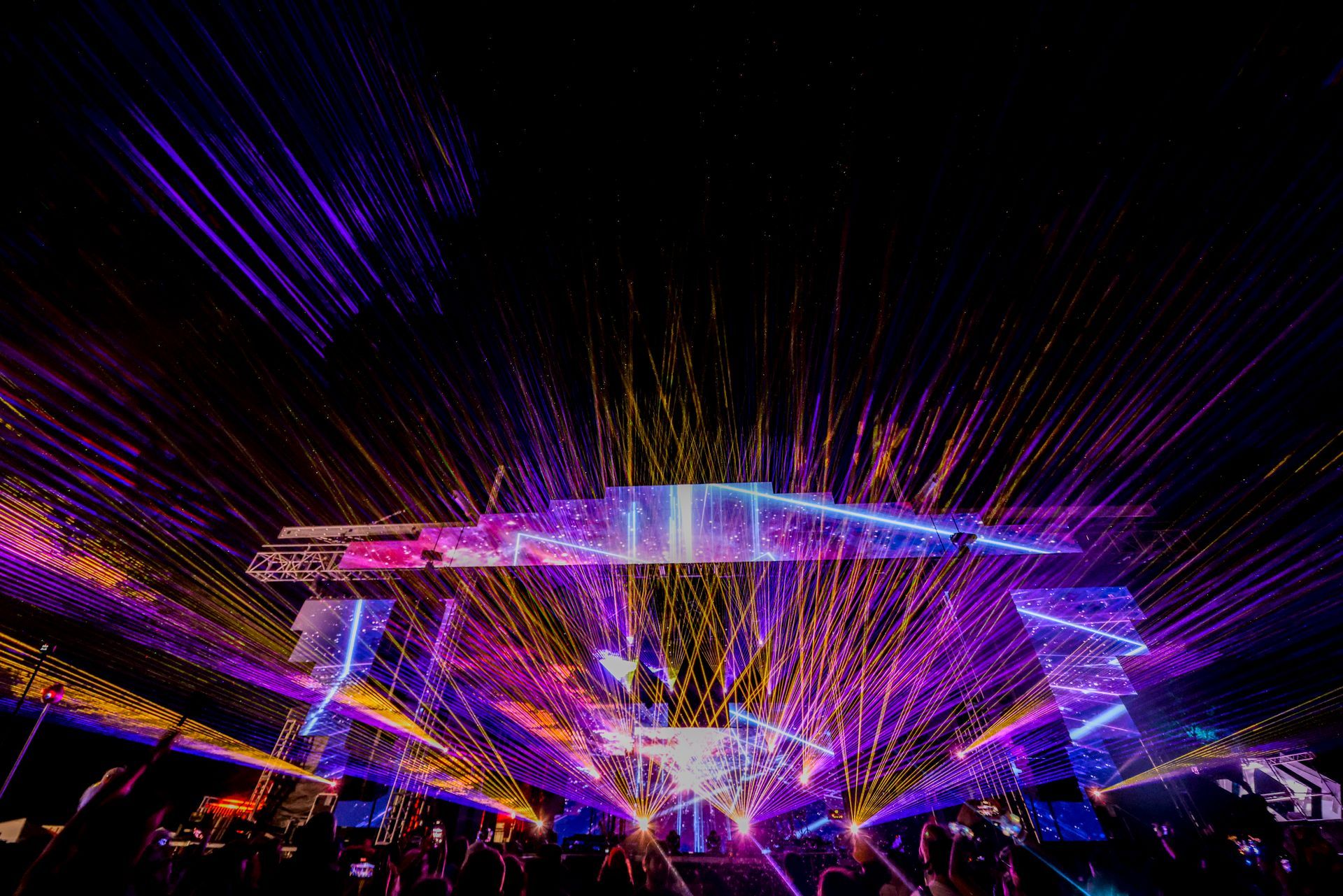 A crowd of people are watching a concert with a lot of lights on the stage.