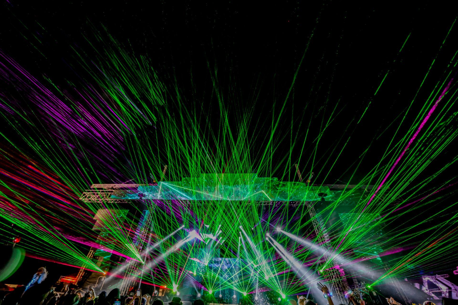 A crowd of people are watching a concert with a lot of lights coming out of the stage.
