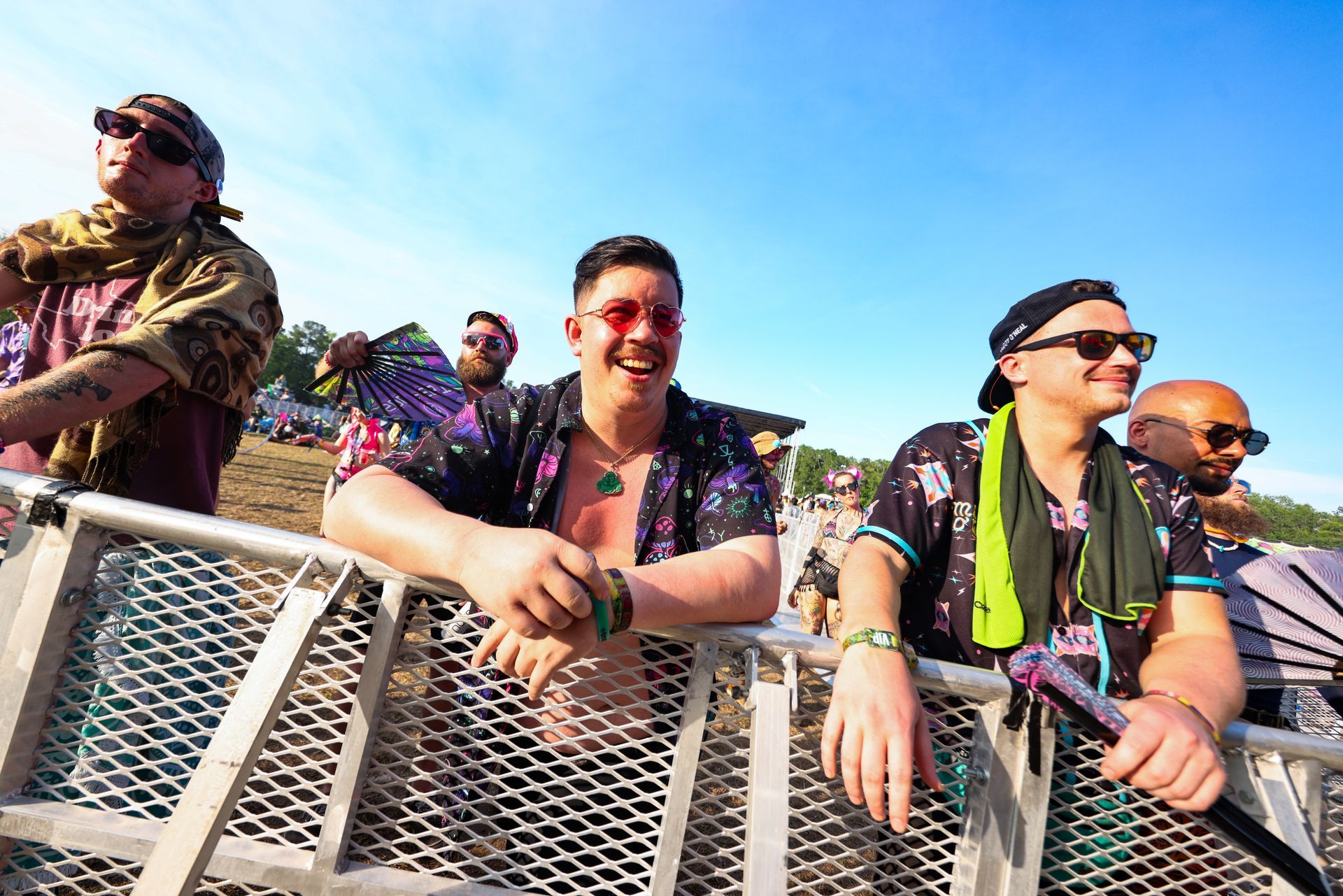 A group of men are leaning on a metal fence at a music festival.