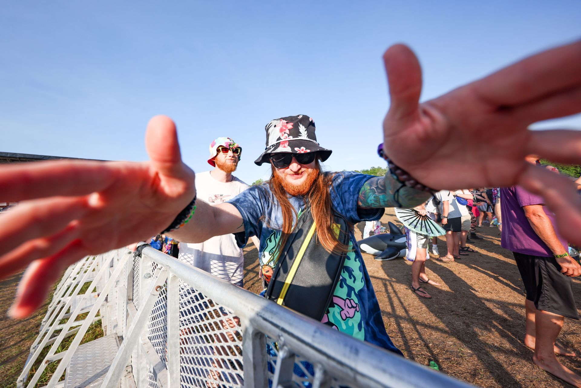 A woman wearing a hat and sunglasses is reaching out towards a crowd of people.