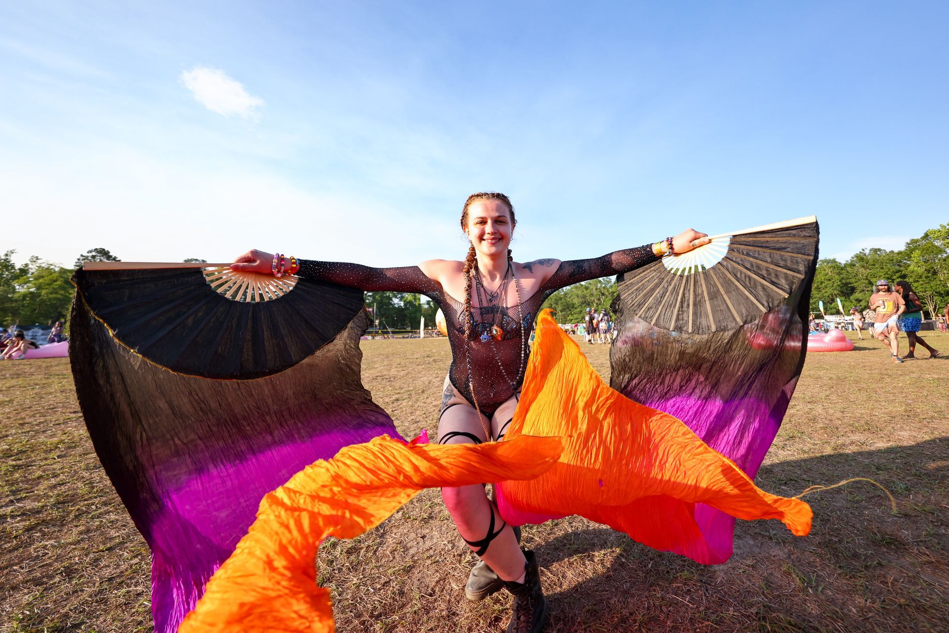 A woman is holding a pair of fans in a field.