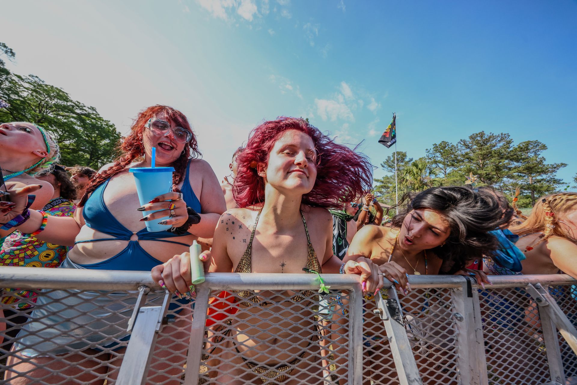 A group of women are standing behind a metal fence at a music festival.