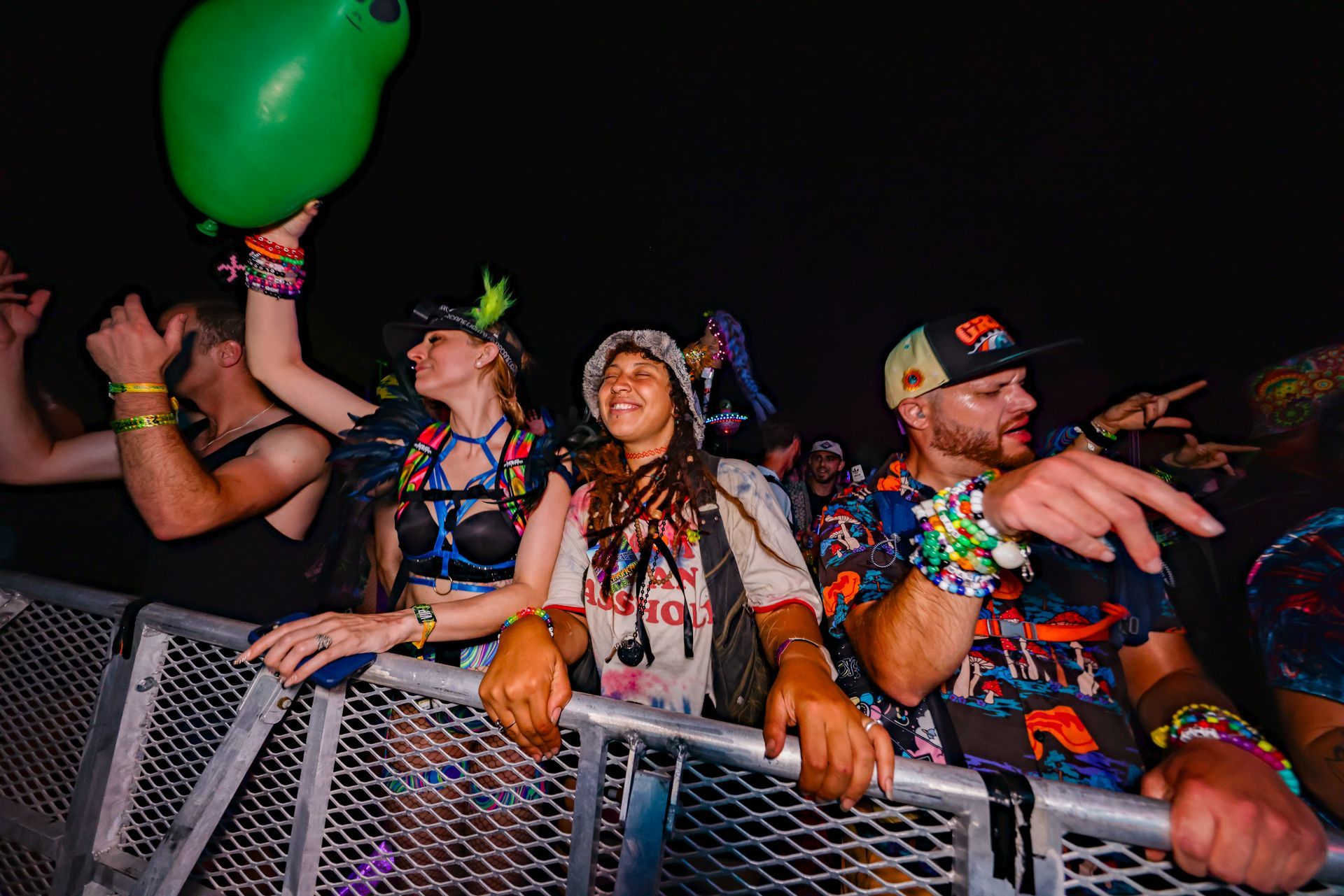 A group of people are standing behind a fence at a concert holding balloons.