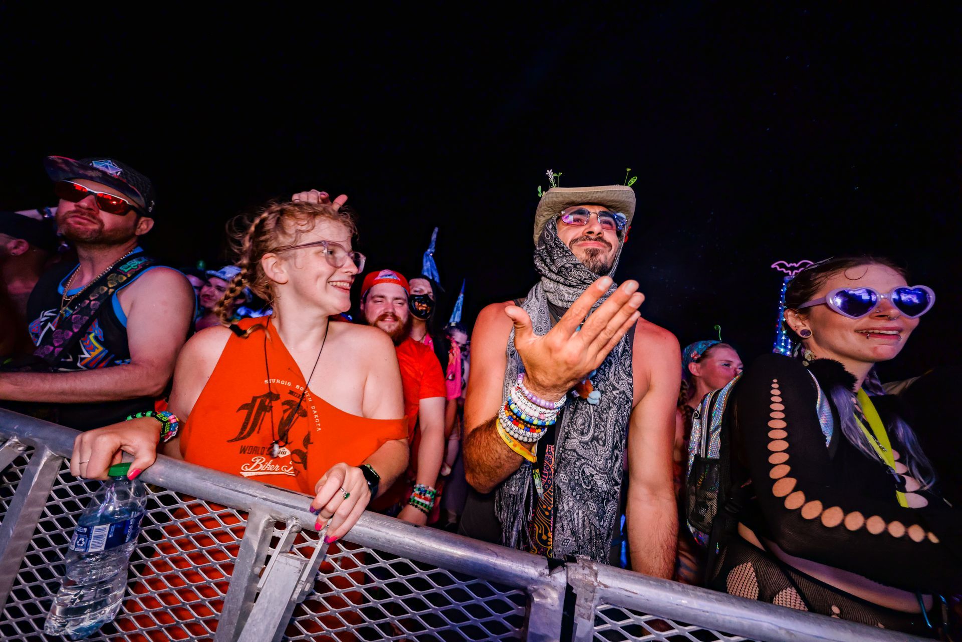 A group of people are standing behind a metal fence at a concert.