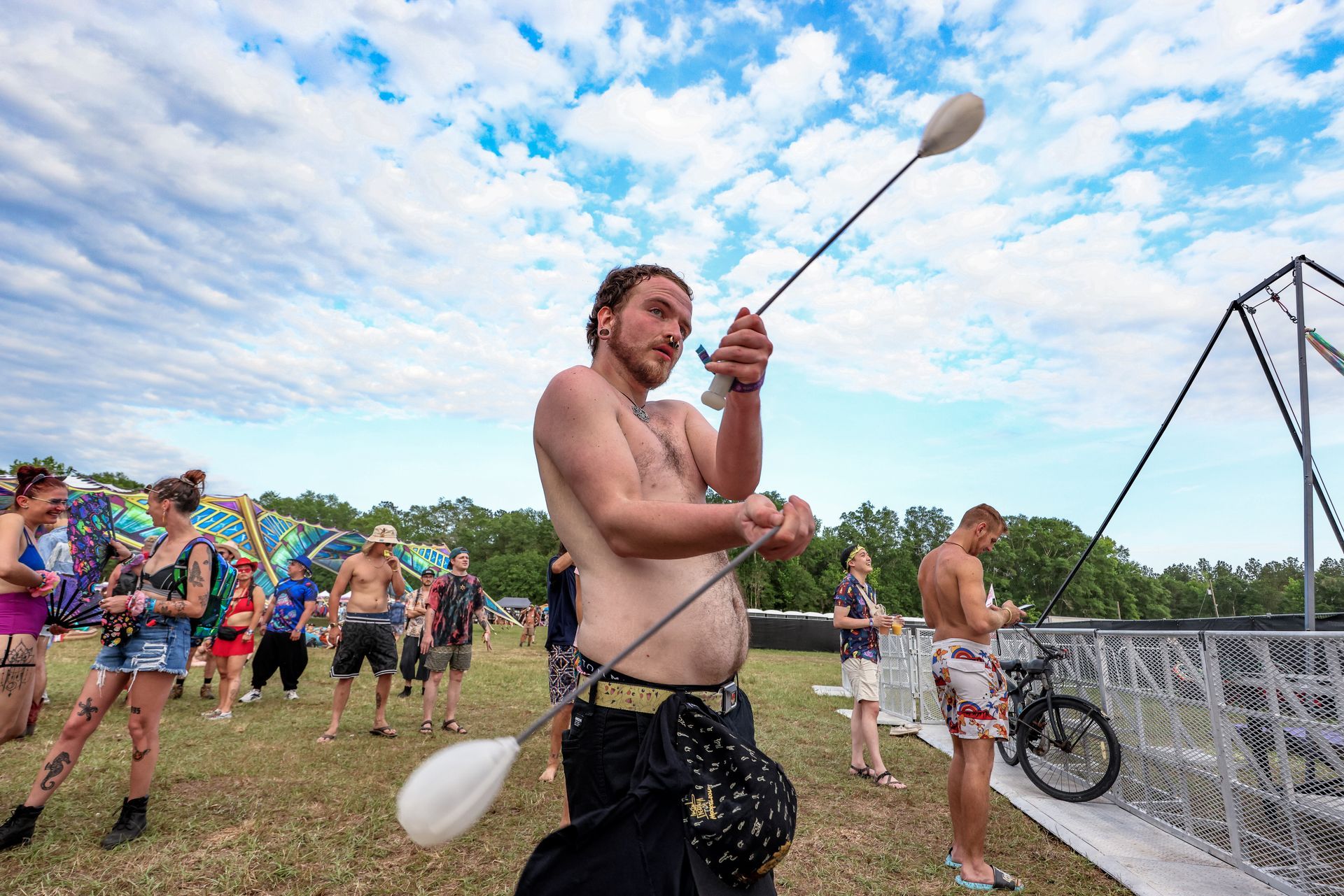 A shirtless man is juggling a stick in a field.