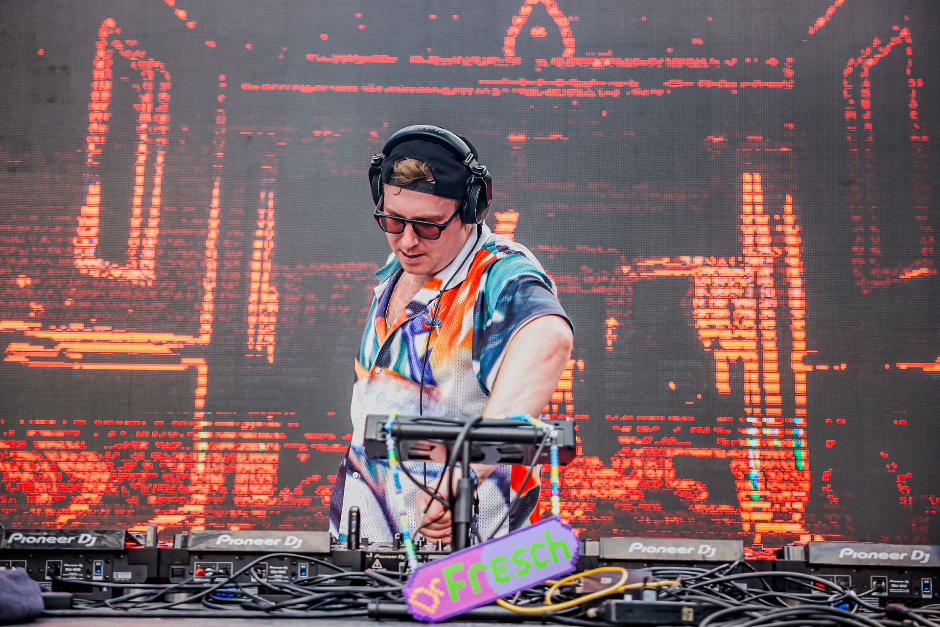 A man is playing a dj set in front of a large screen.