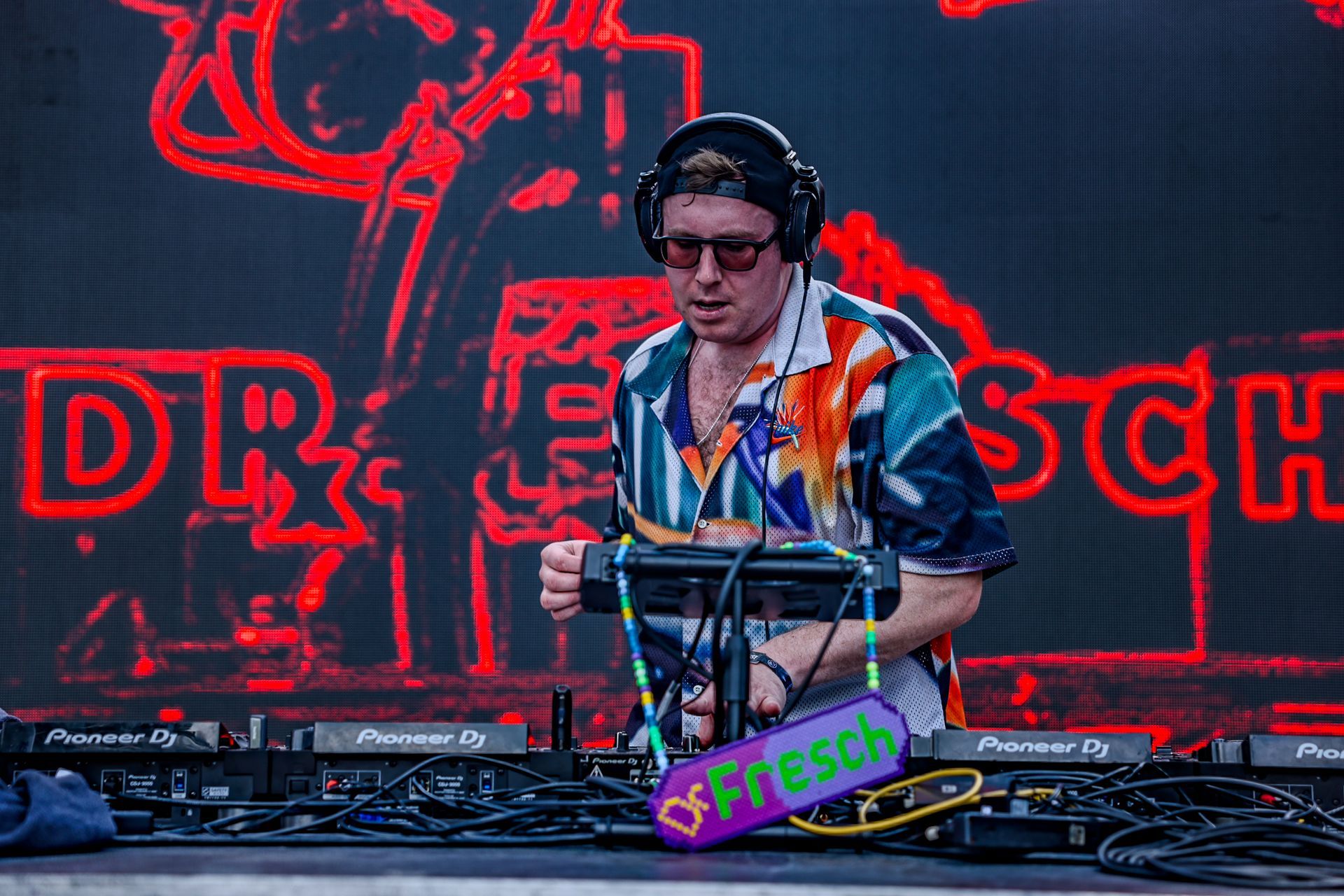 A man wearing headphones and sunglasses is playing a dj set on a stage.