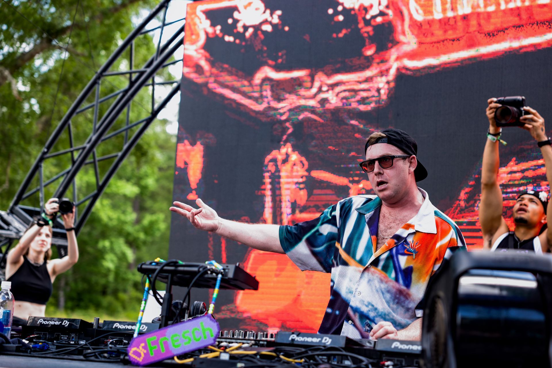 A man is playing a dj set on a stage while people take pictures of him.