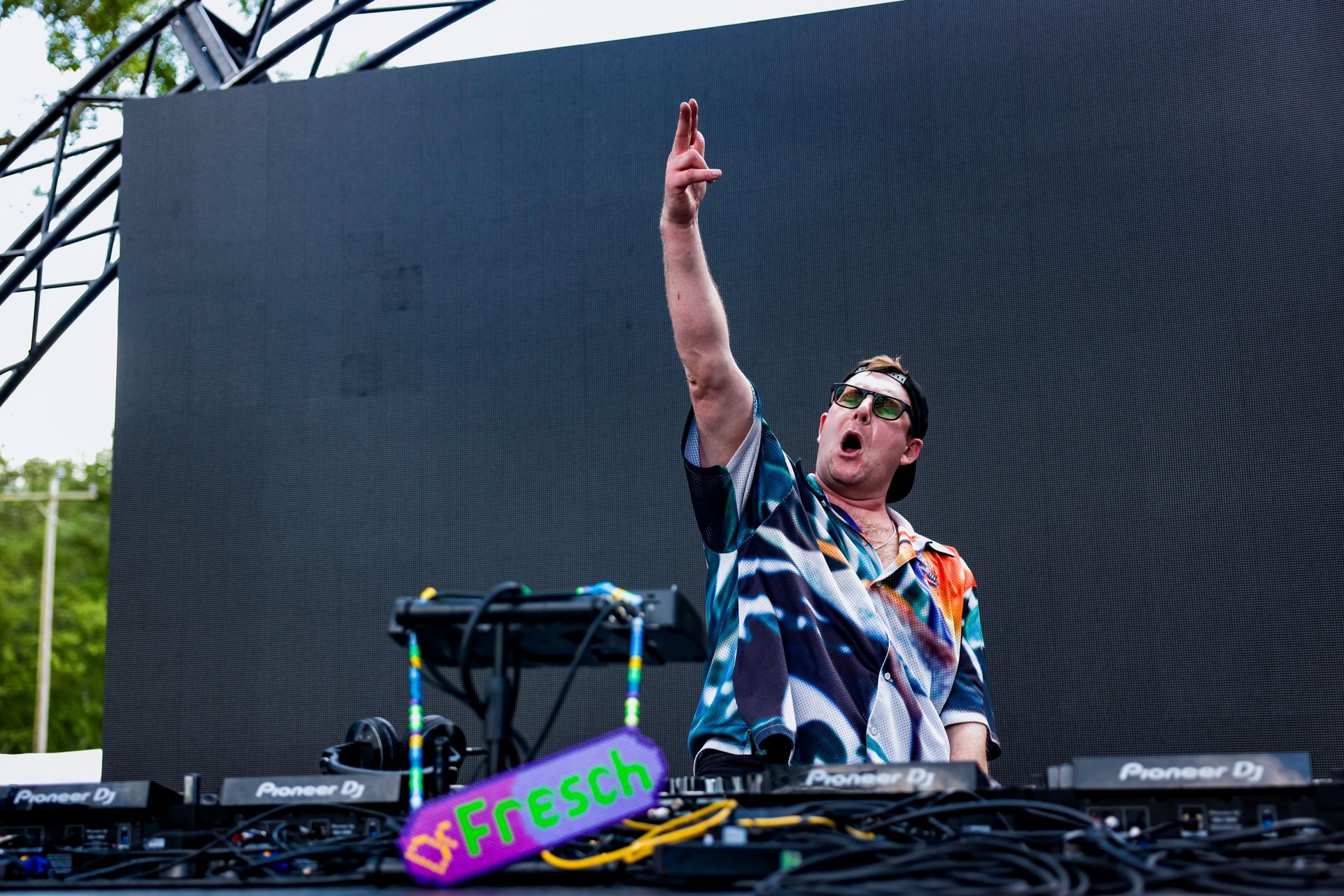 A man is standing in front of a large screen playing a dj set.