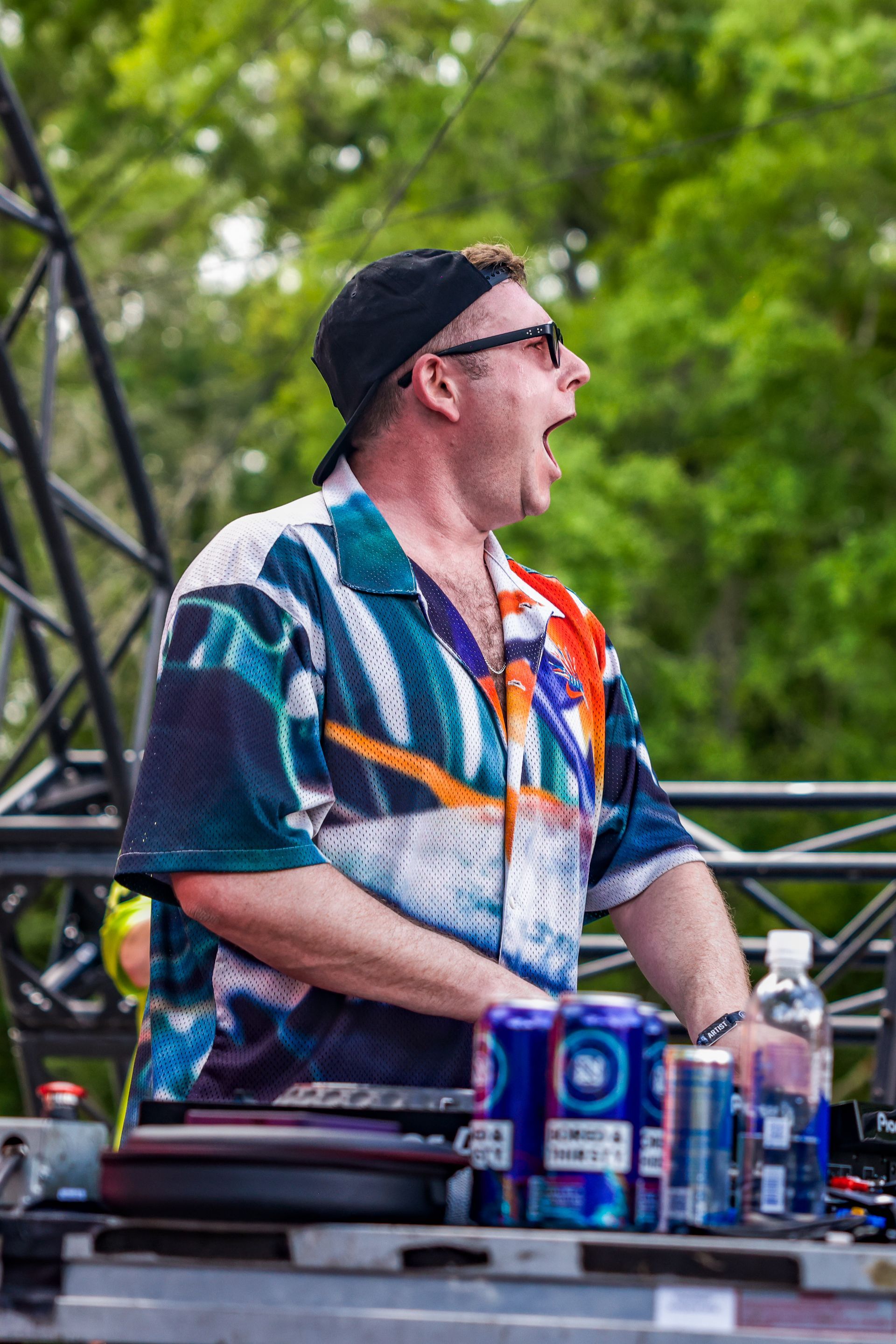 A man in a colorful shirt is standing in front of a dj booth.