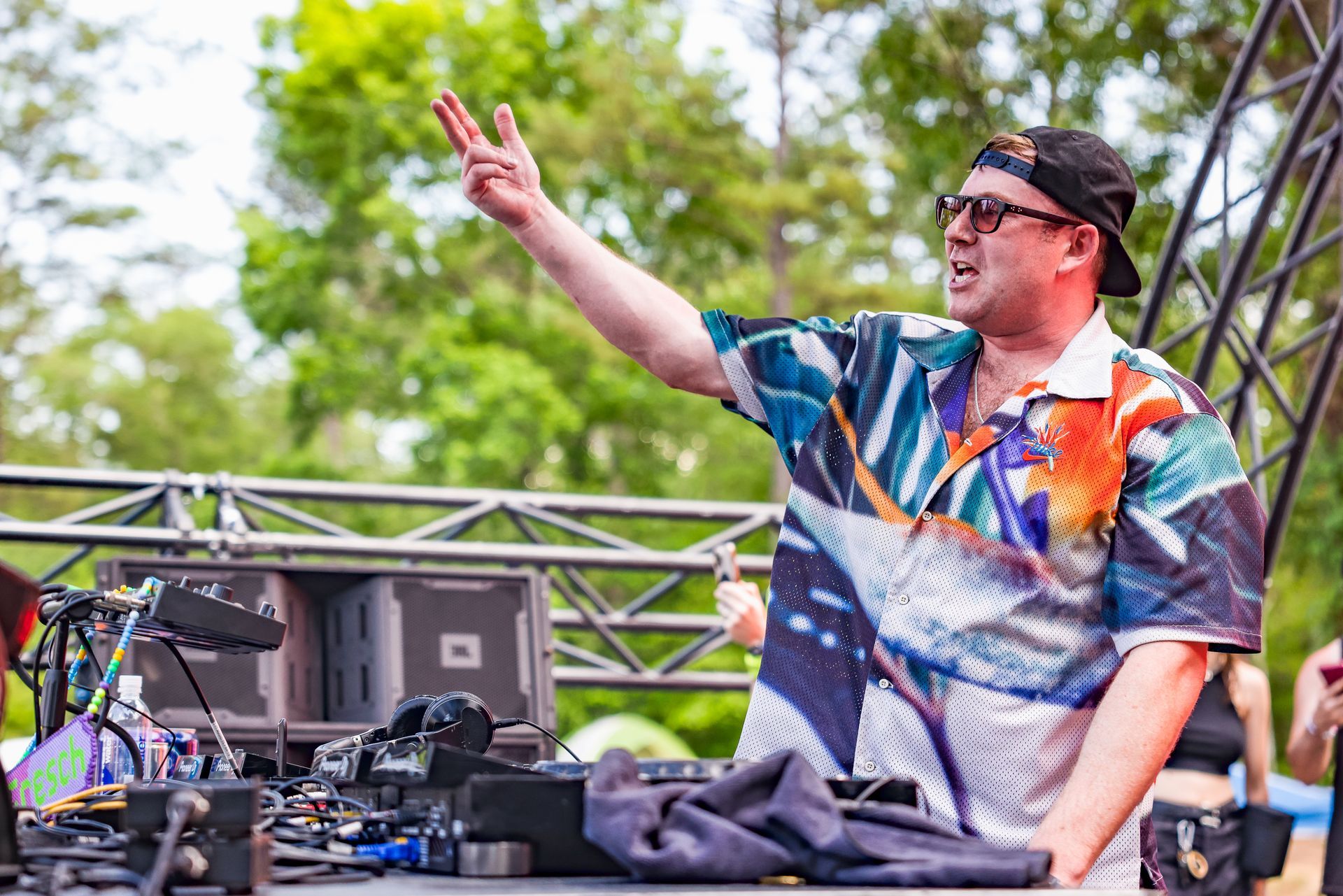 A man in a colorful shirt and hat is standing in front of a stage.