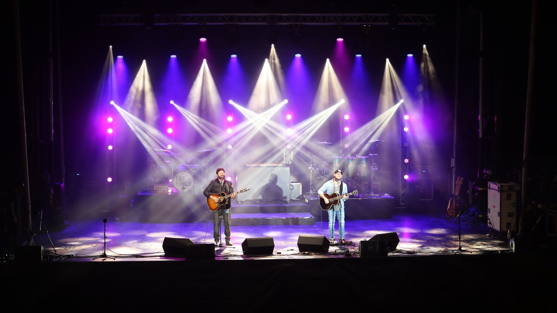 Two men are playing guitars on a stage with purple lights