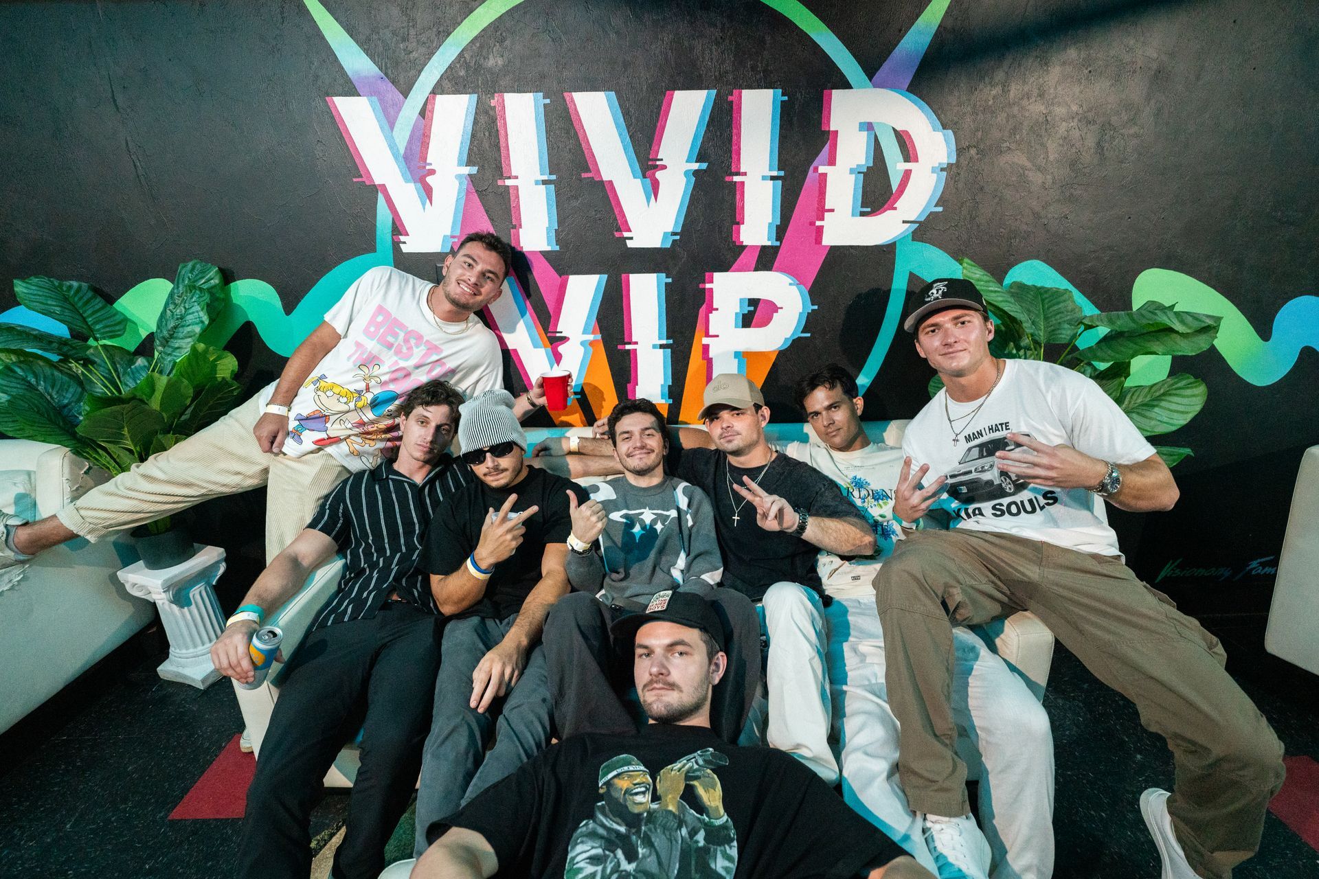A group of young men are posing for a picture in front of a wall that says vivid vip.