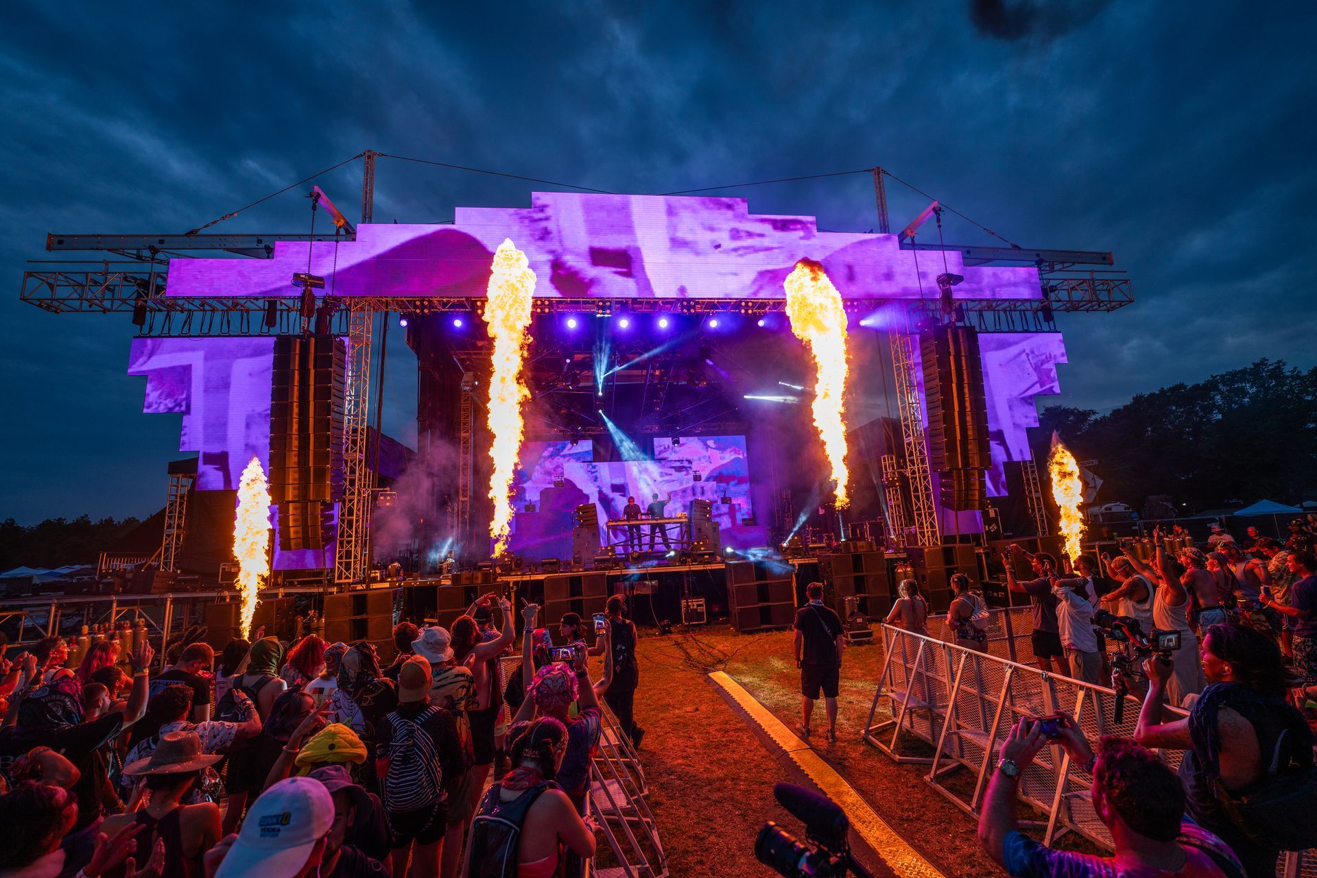 A crowd of people are standing in front of a stage at a music festival.