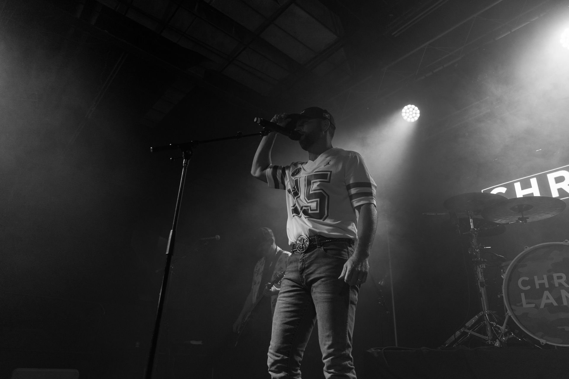 A man is singing into a microphone on a stage in a black and white photo.
