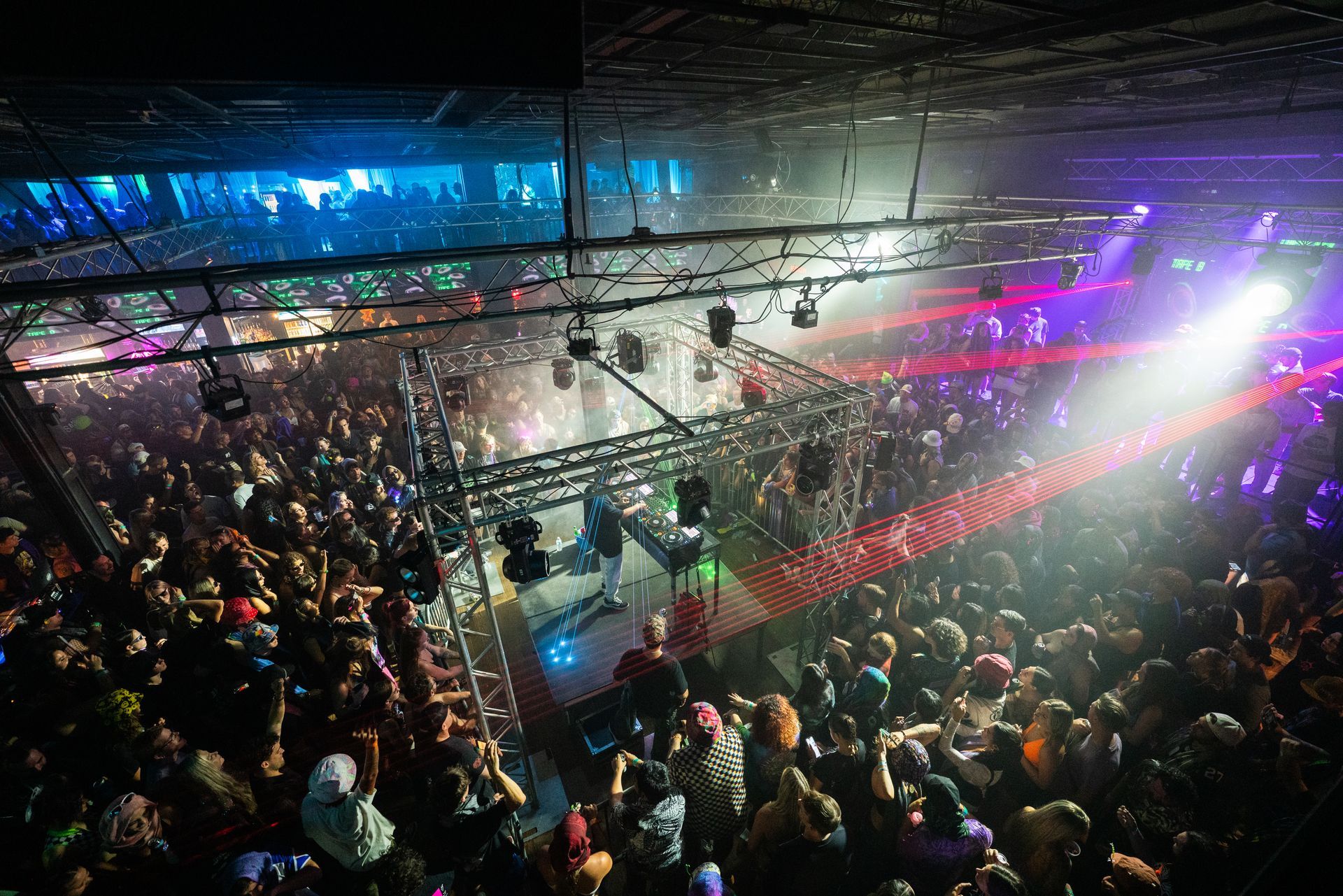 A large crowd of people are standing in a dark room at a concert.