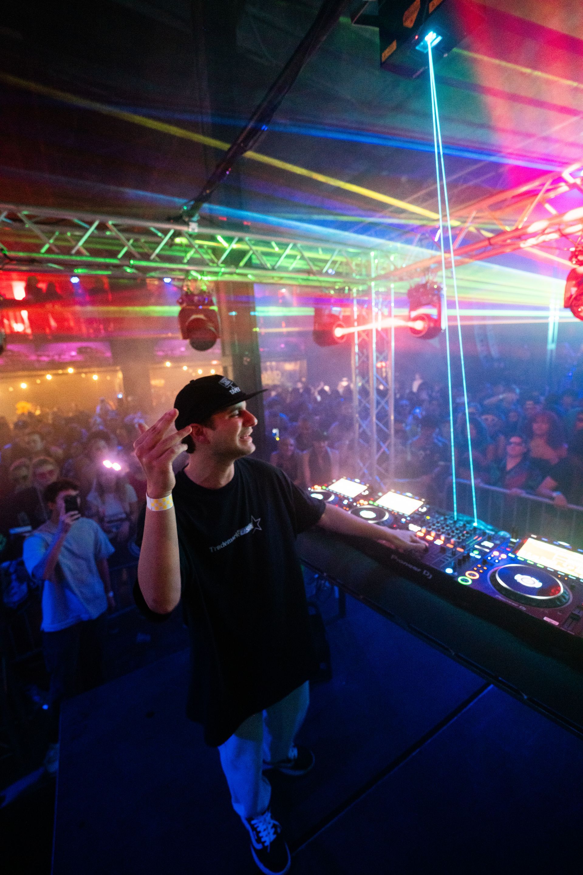A man is standing in front of a dj booth in a club.