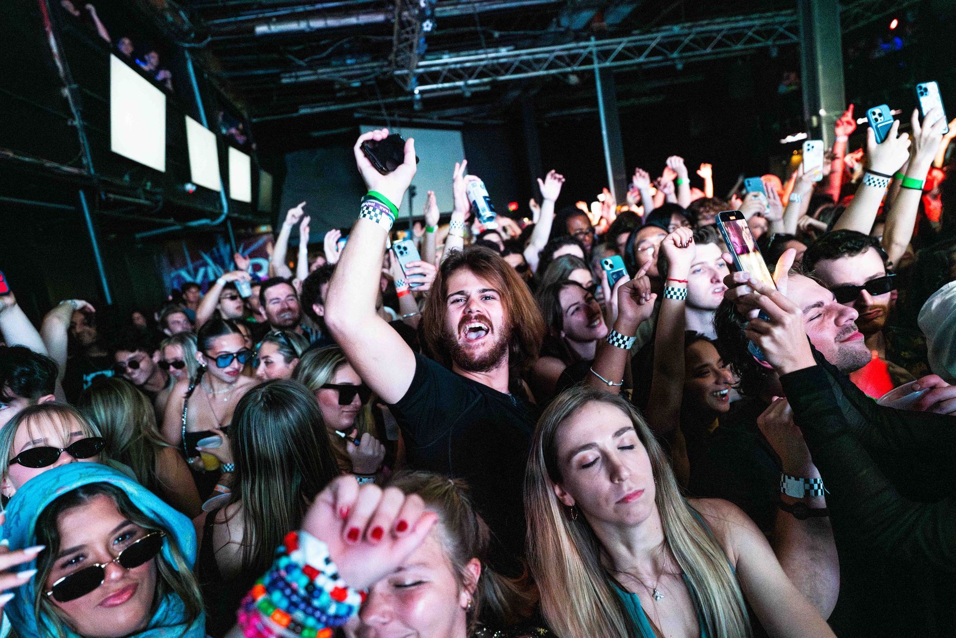 A crowd of people are standing in a room with their hands in the air.