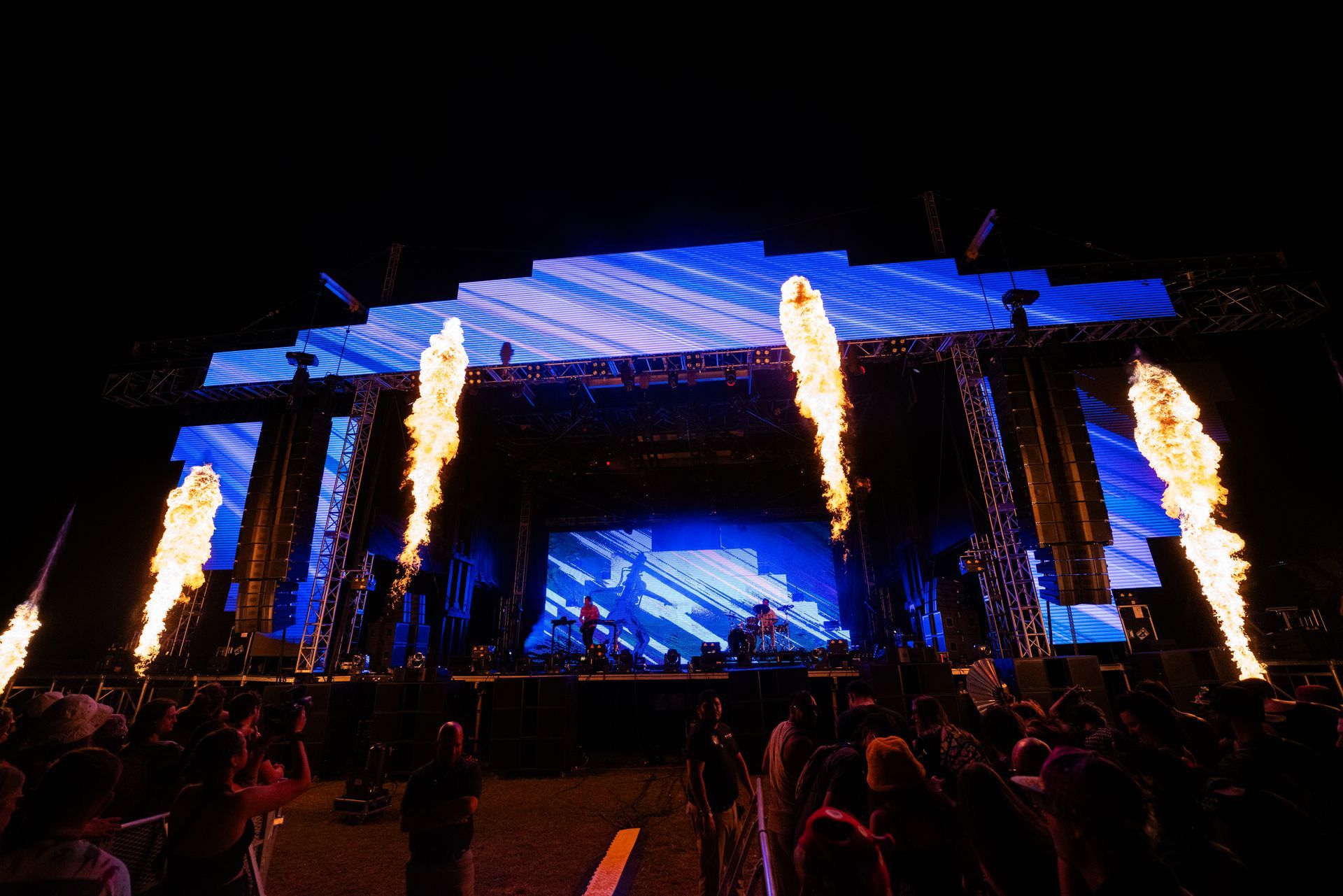 A crowd of people are standing in front of a stage with flames coming out of it.