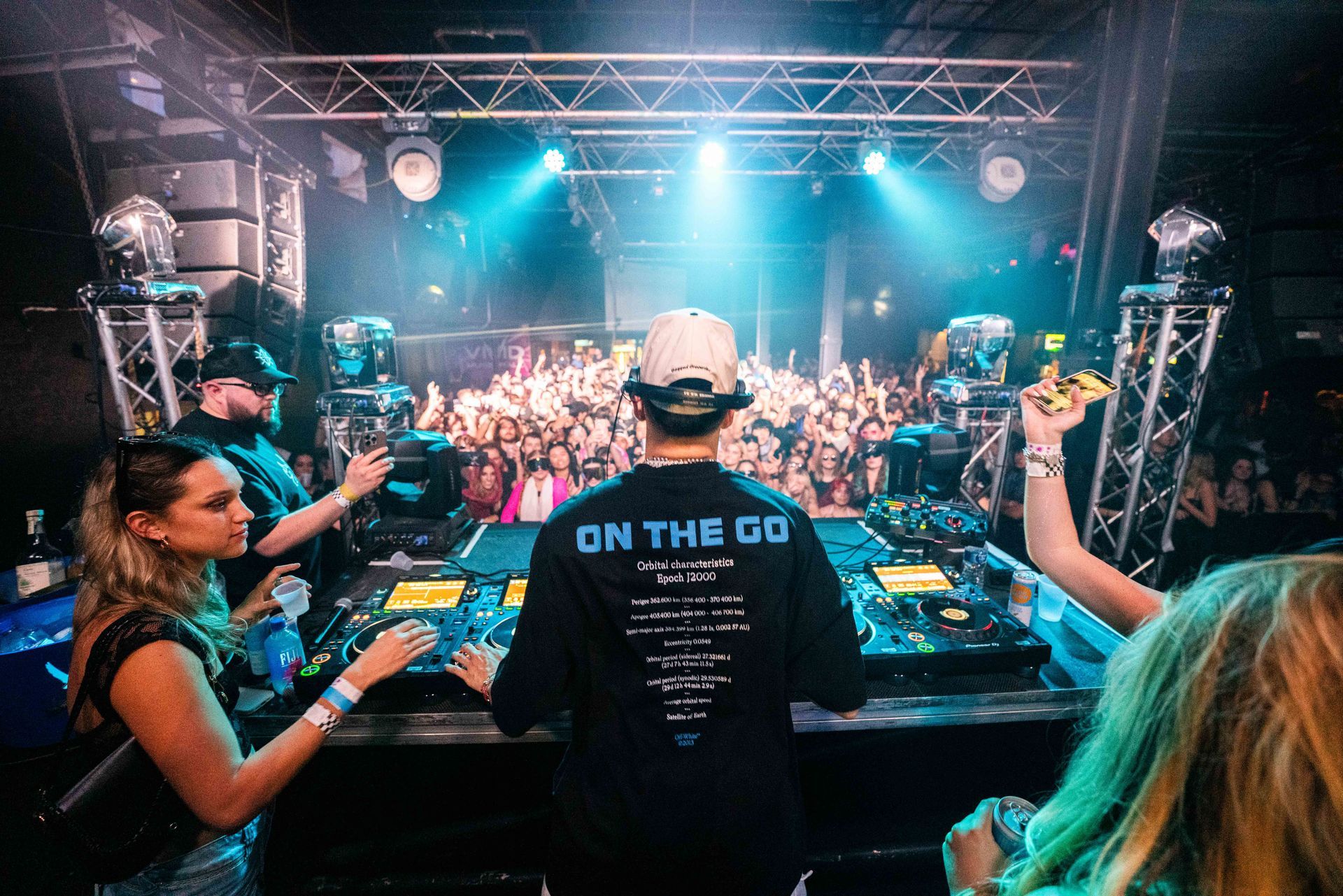 A group of people are standing in front of a dj at a concert.