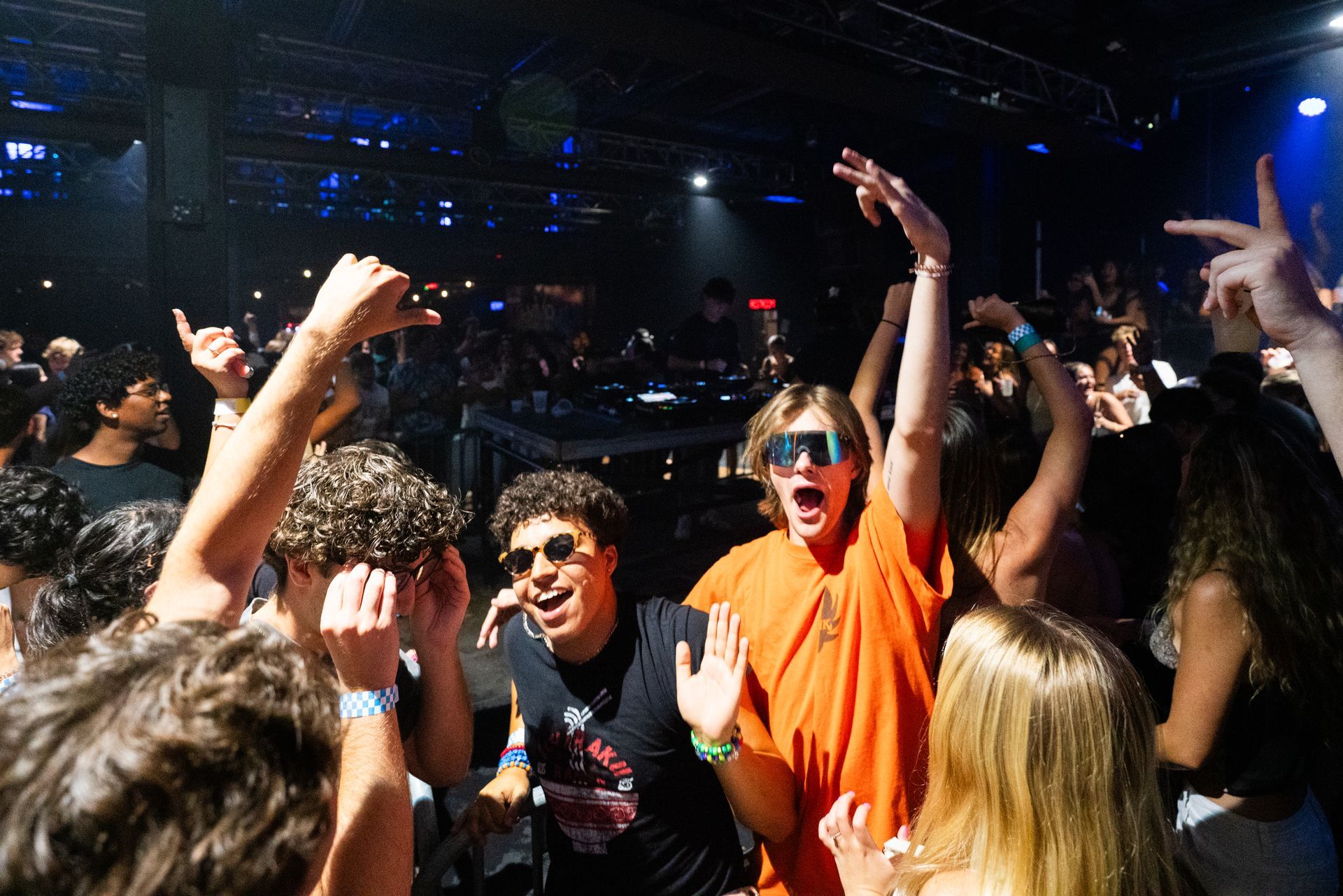 A crowd of people are dancing in a club with their hands in the air.