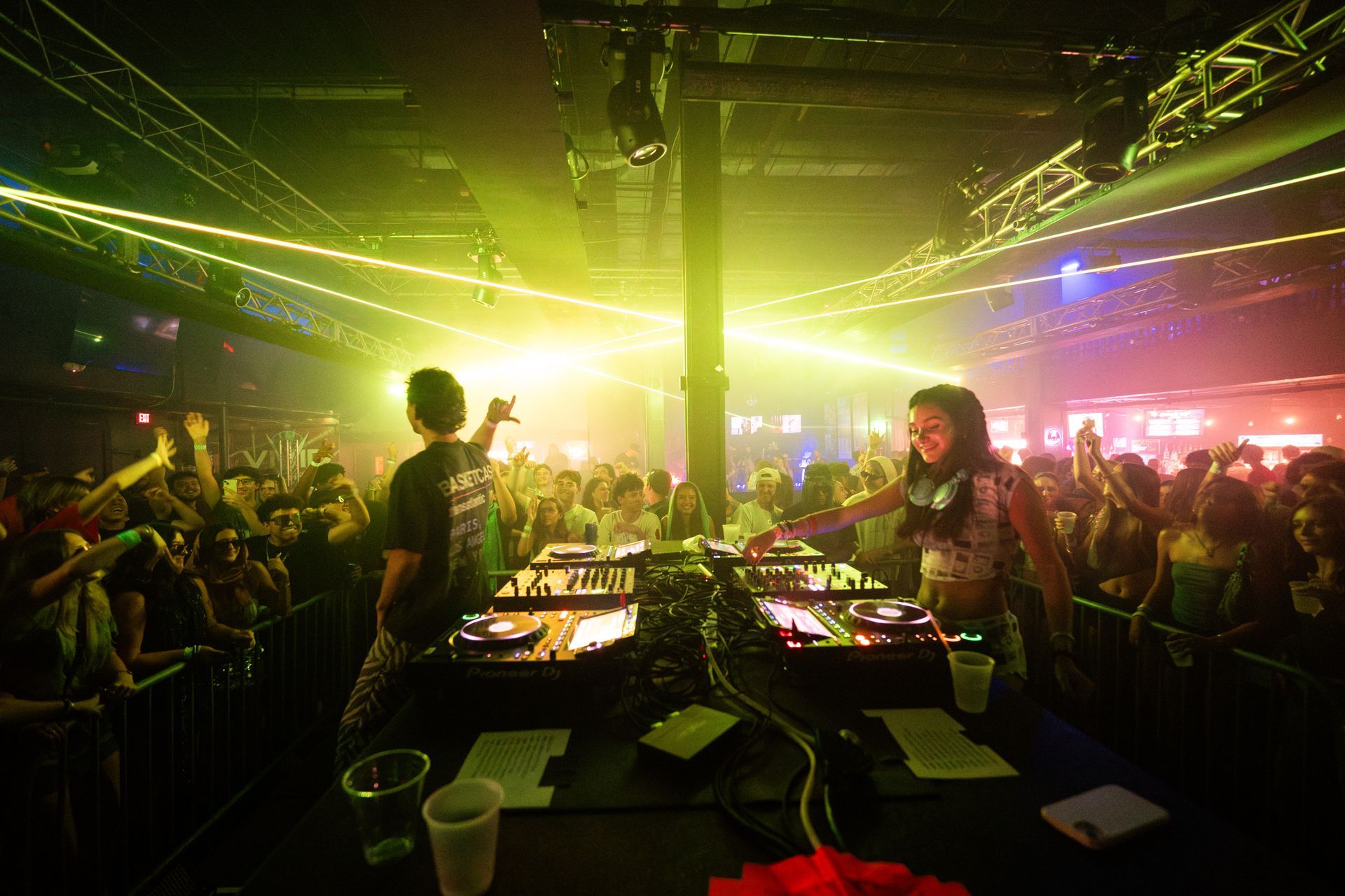 Two djs are playing music in front of a crowd at a club.