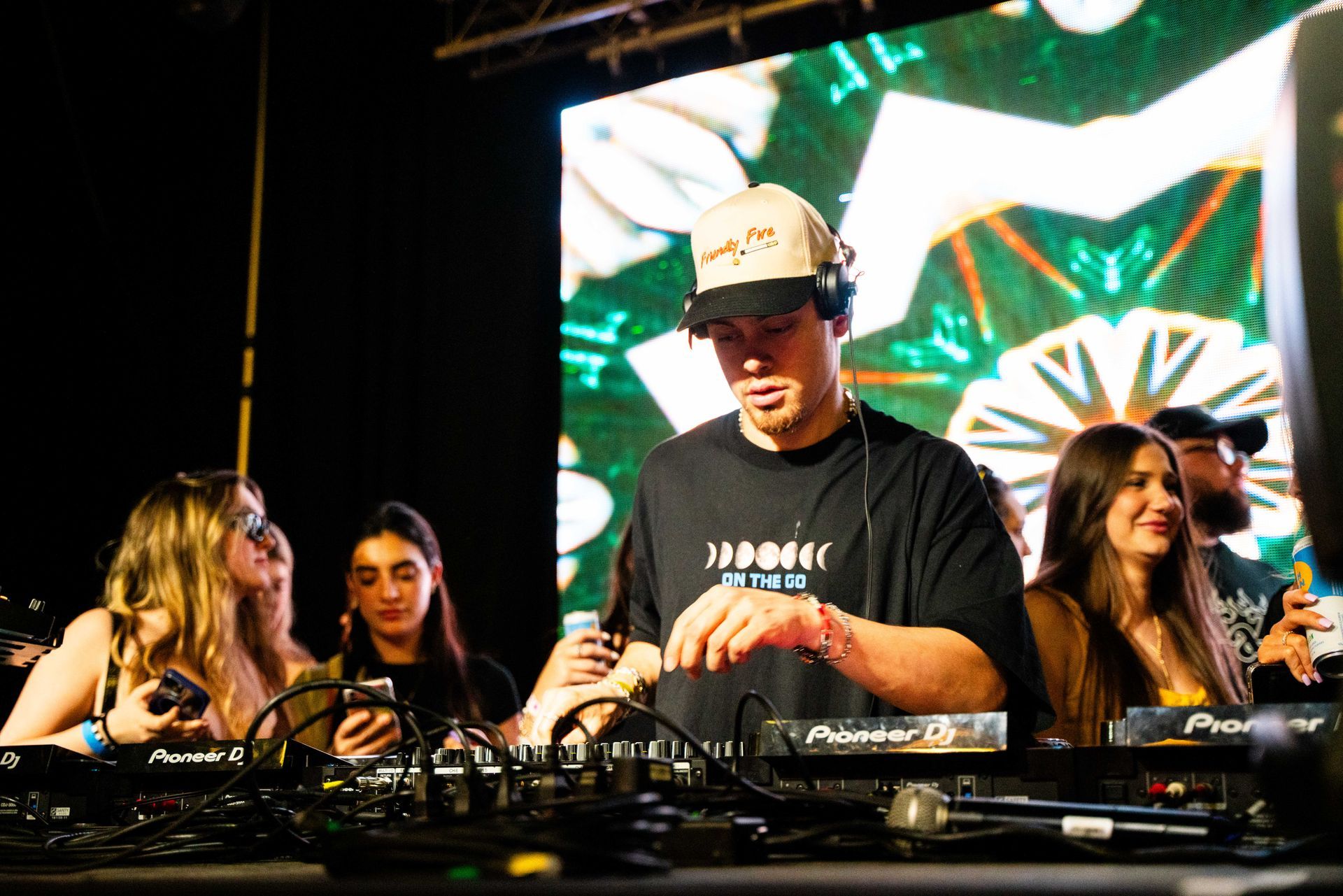 A group of people are standing around a dj on a stage.