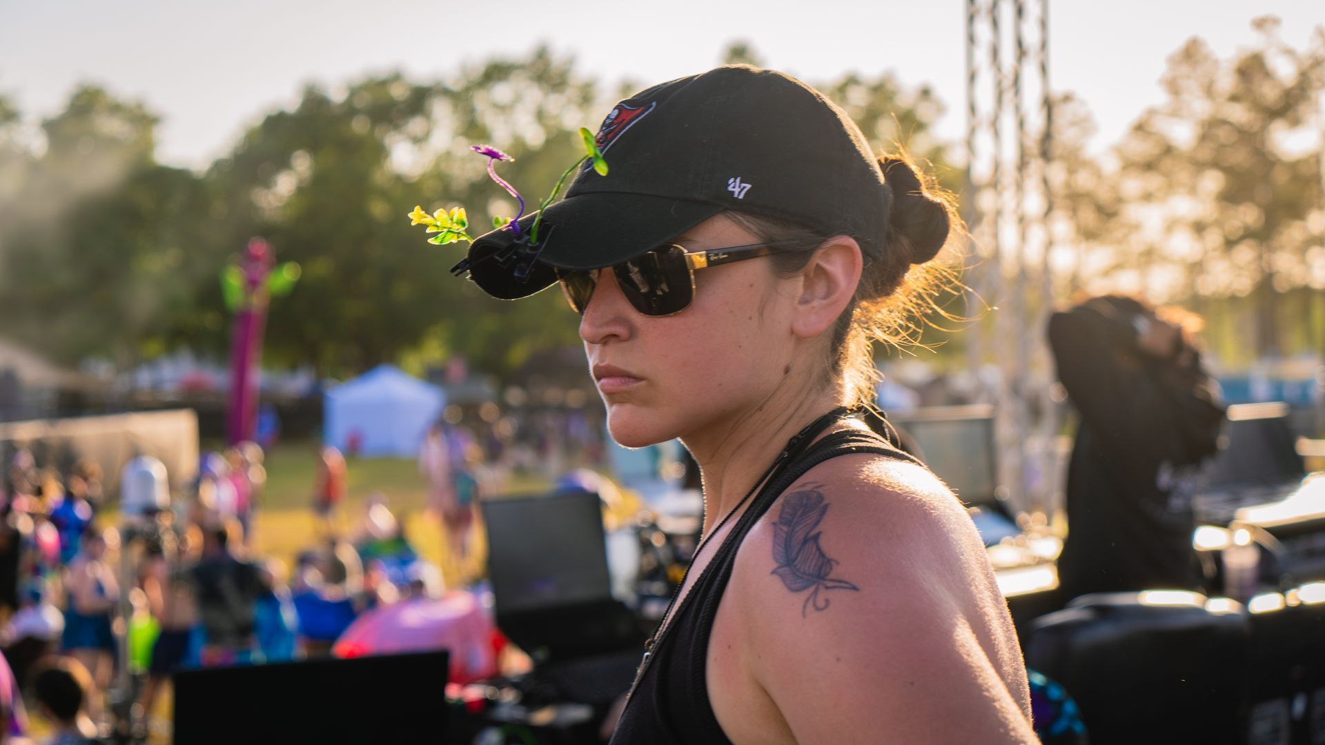 A woman wearing a hat and sunglasses is standing in front of a crowd at a festival.