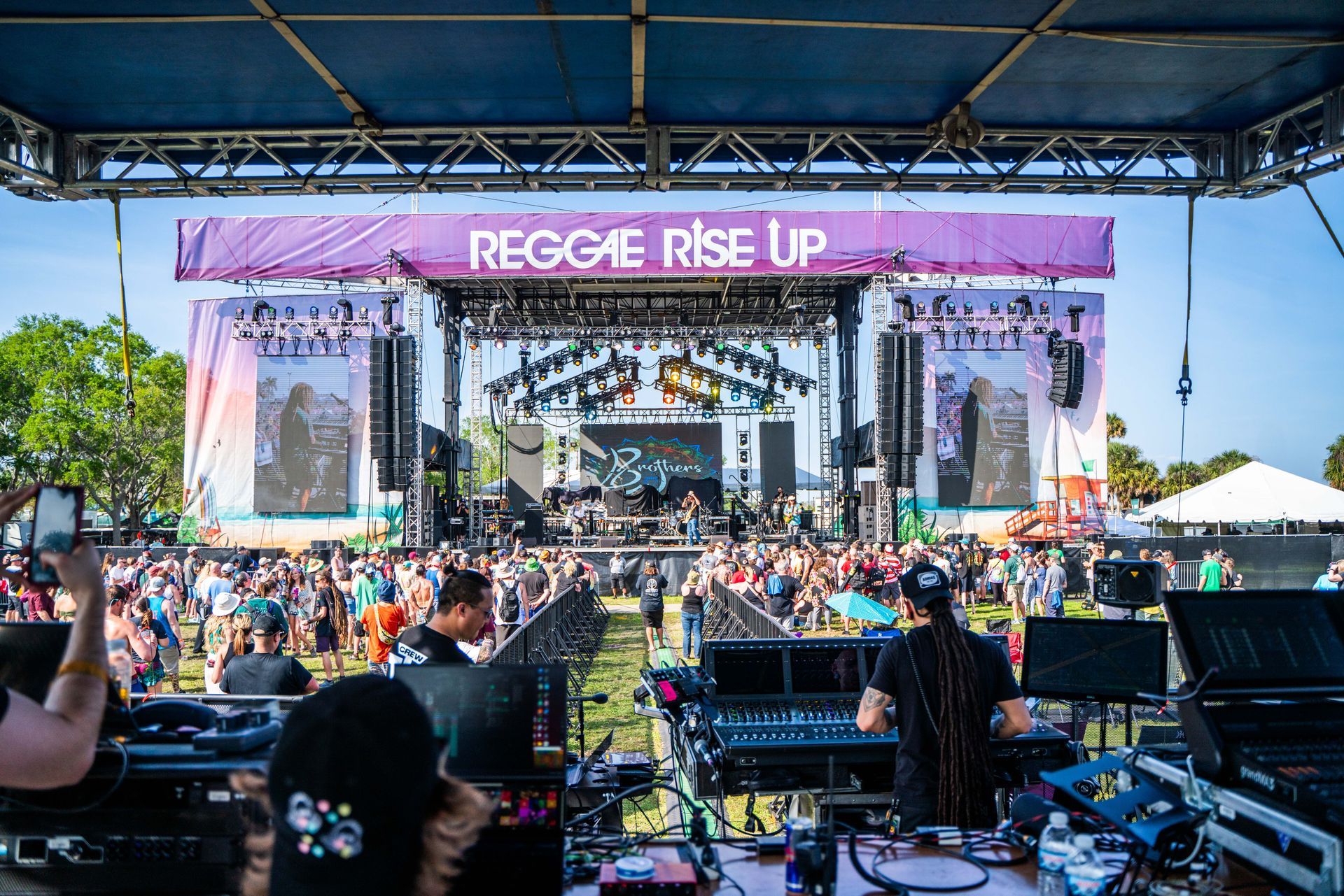 A large crowd of people are gathered in front of a stage at a music festival.