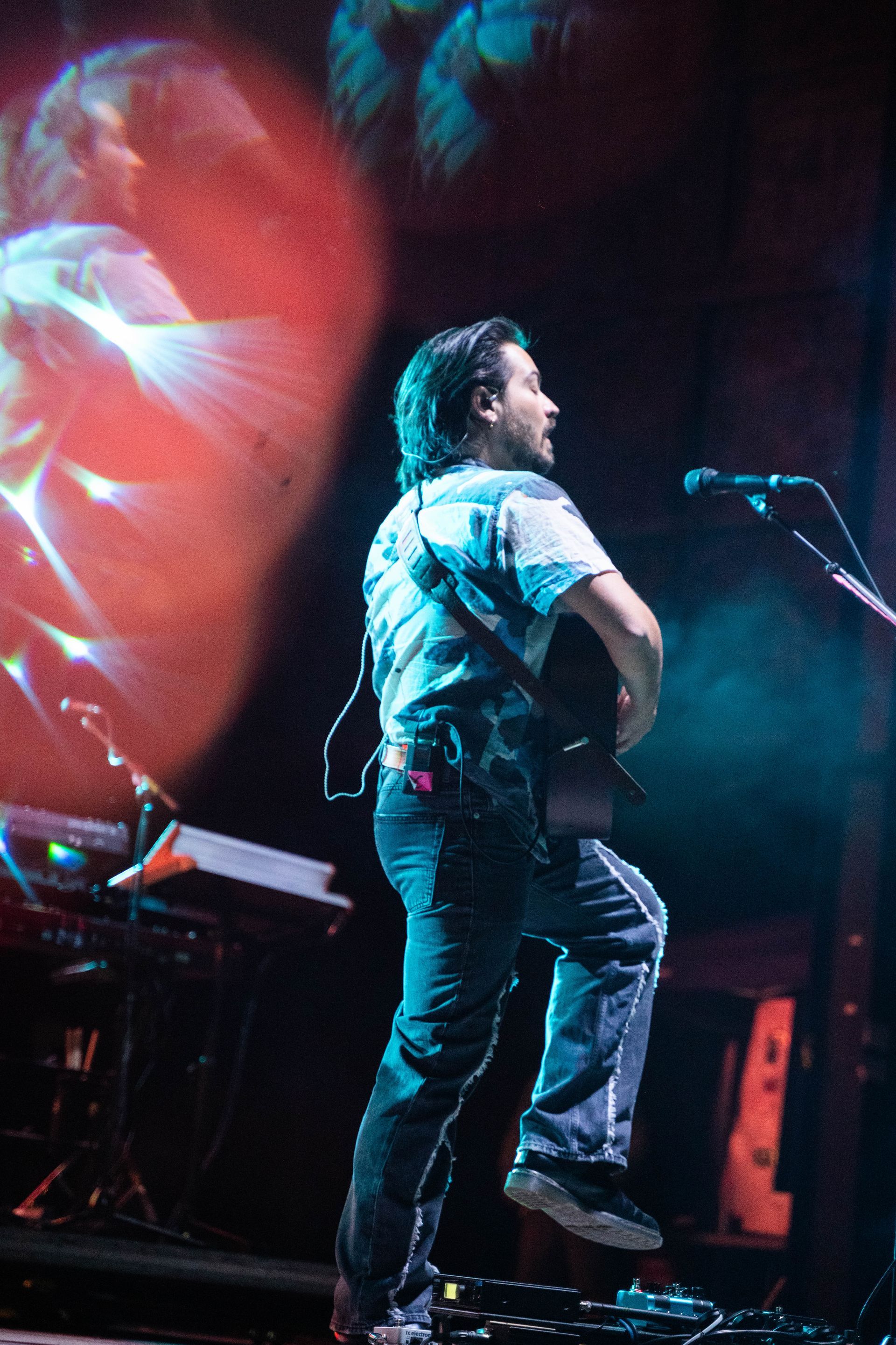 A man playing a guitar and singing into a microphone on a stage