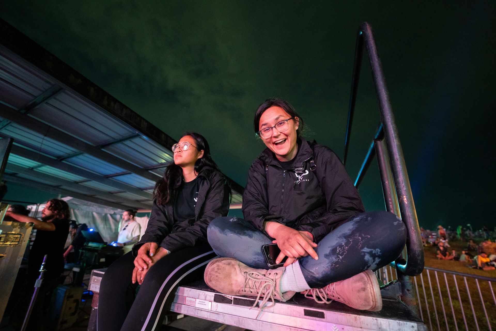 Two girls are sitting on a stage at a concert.