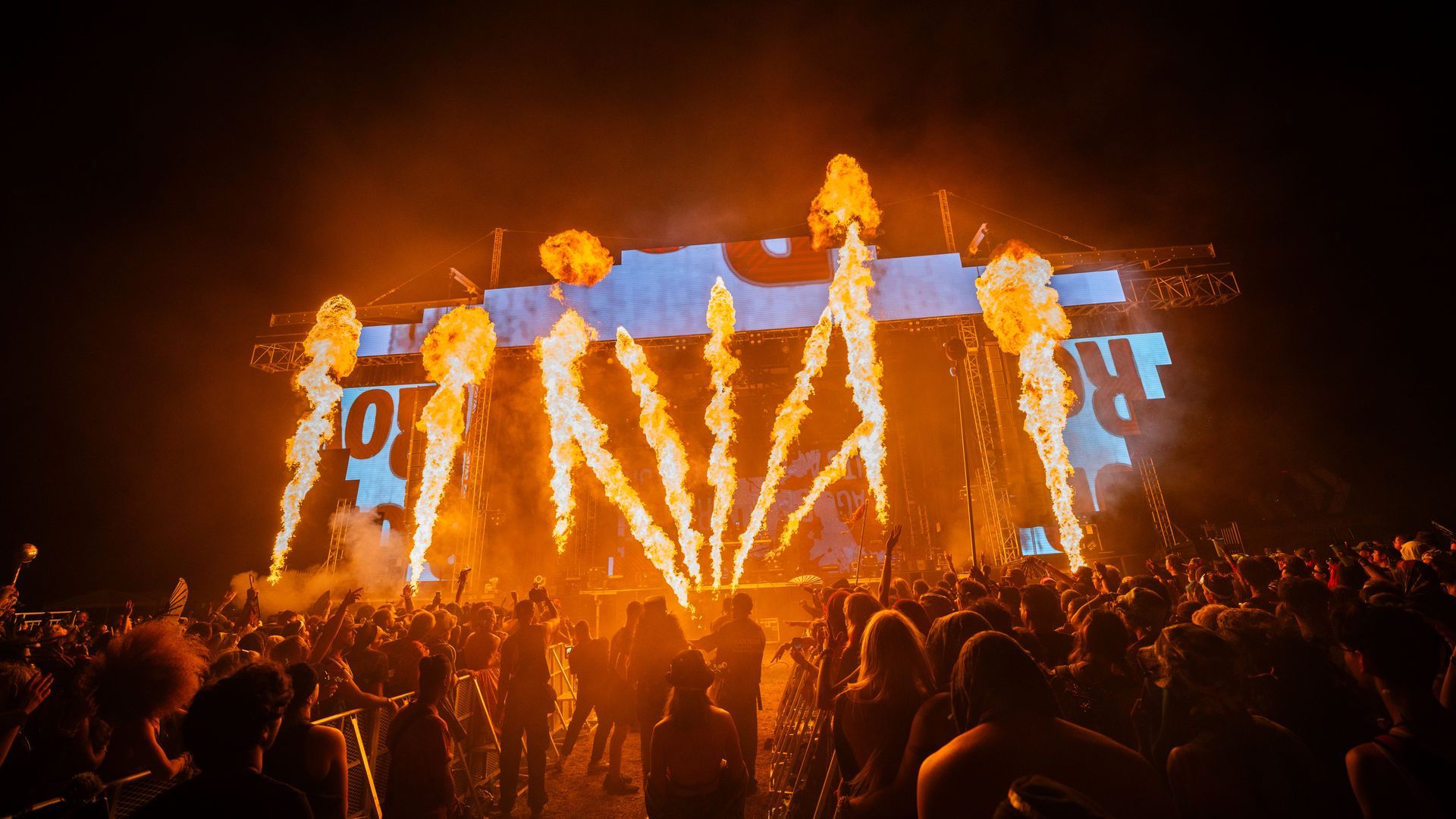 A crowd of people are standing in front of a stage with fireworks coming out of it.