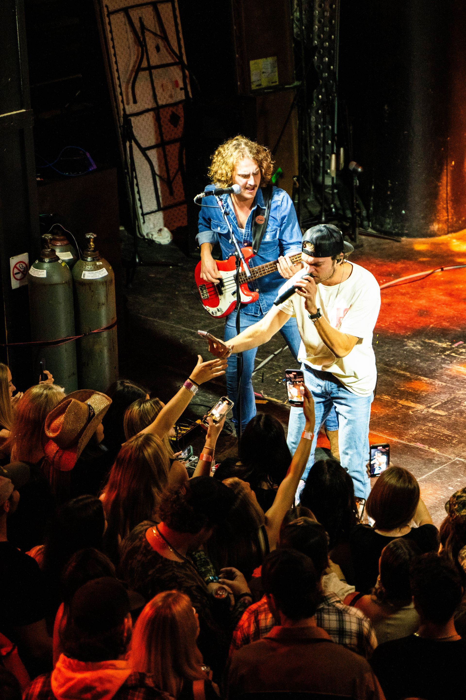 A man is singing into a microphone while another man plays a guitar in front of a crowd.