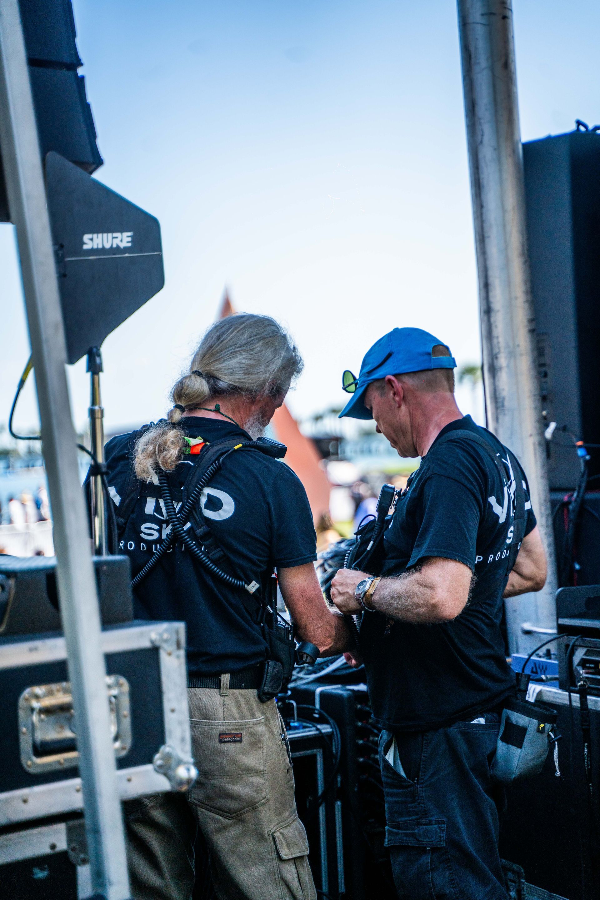 A man in a blue hat is standing next to another man in a black shirt.