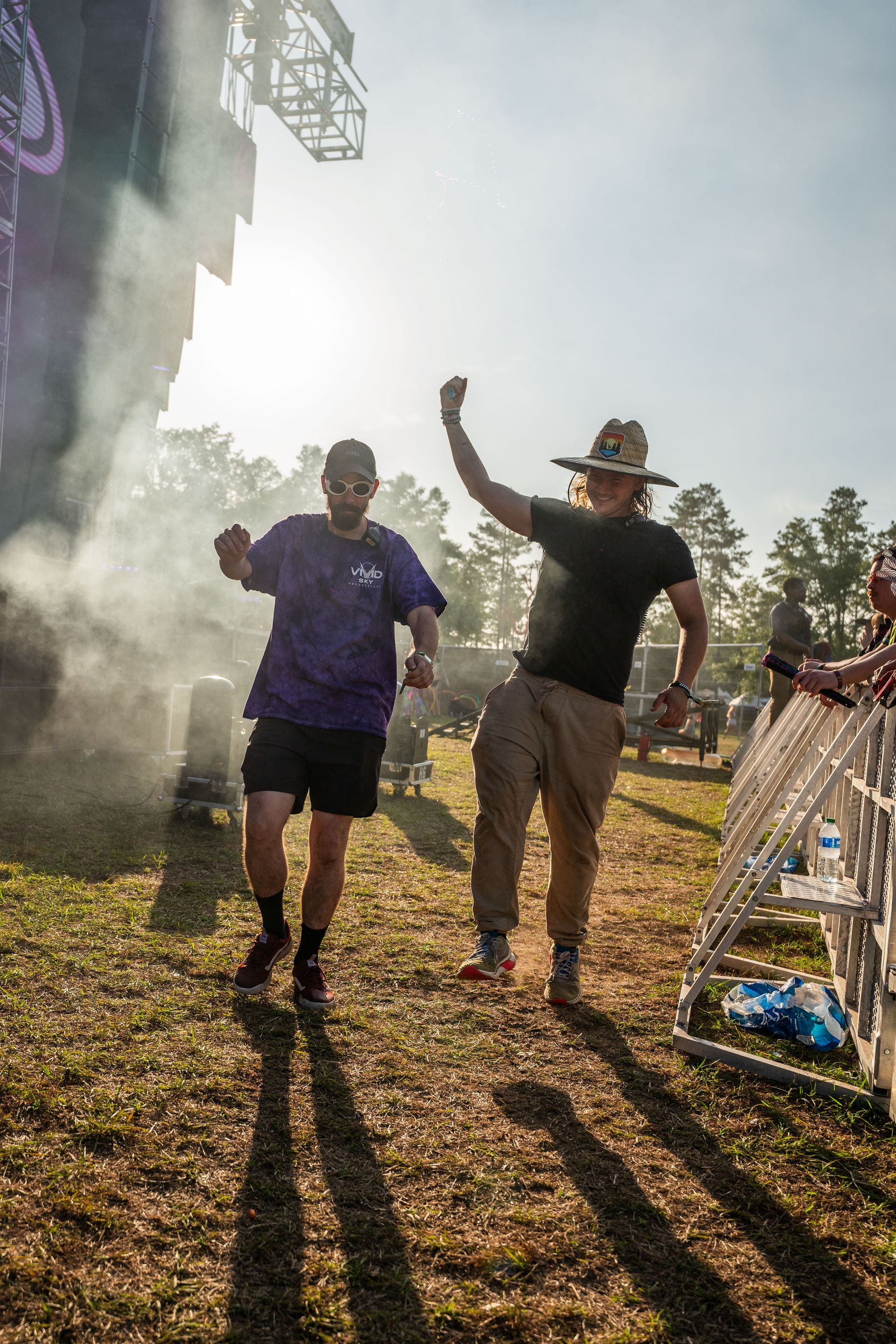 Two men are dancing in a field at a music festival.
