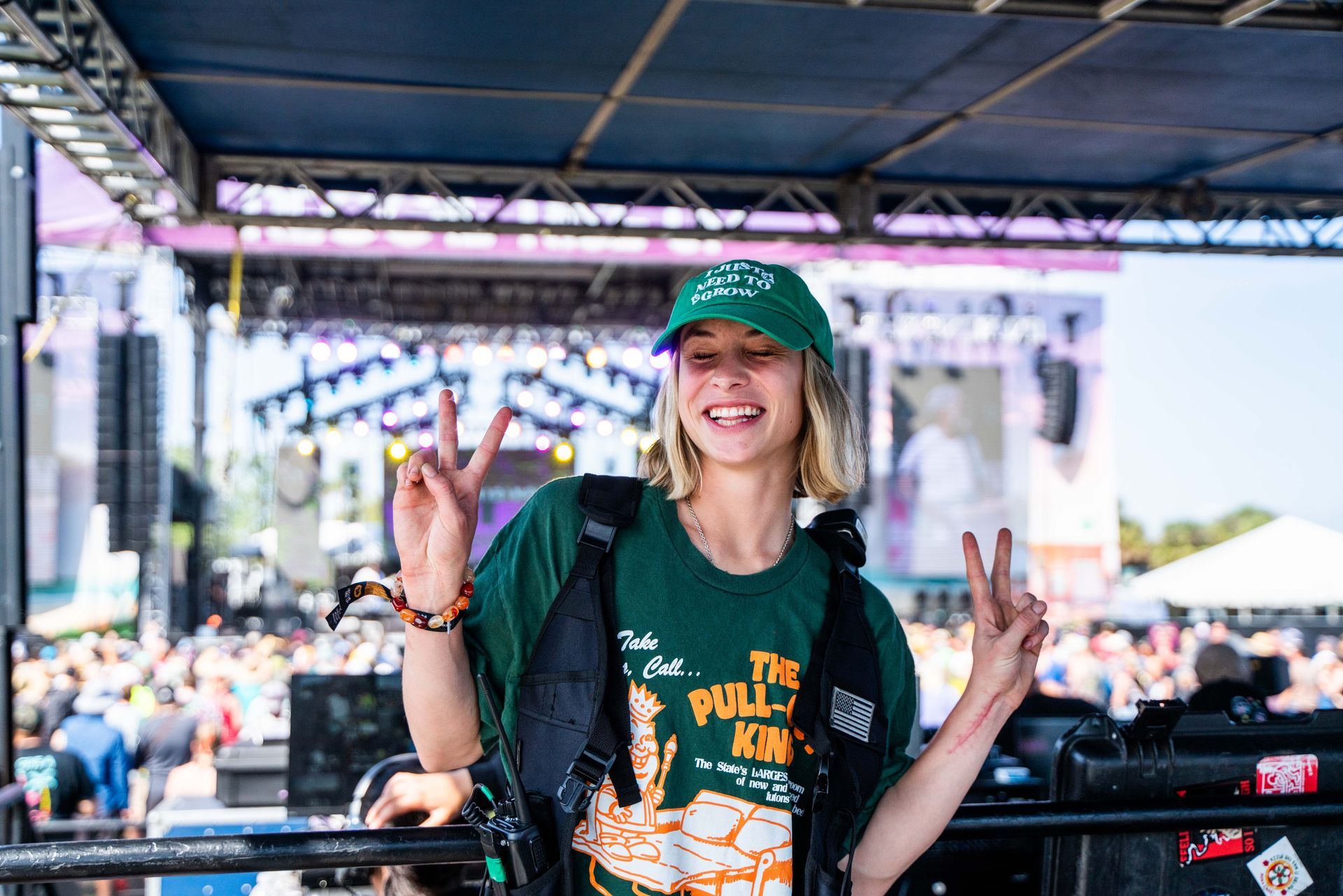 A woman in a green shirt and hat is giving a peace sign at a concert.