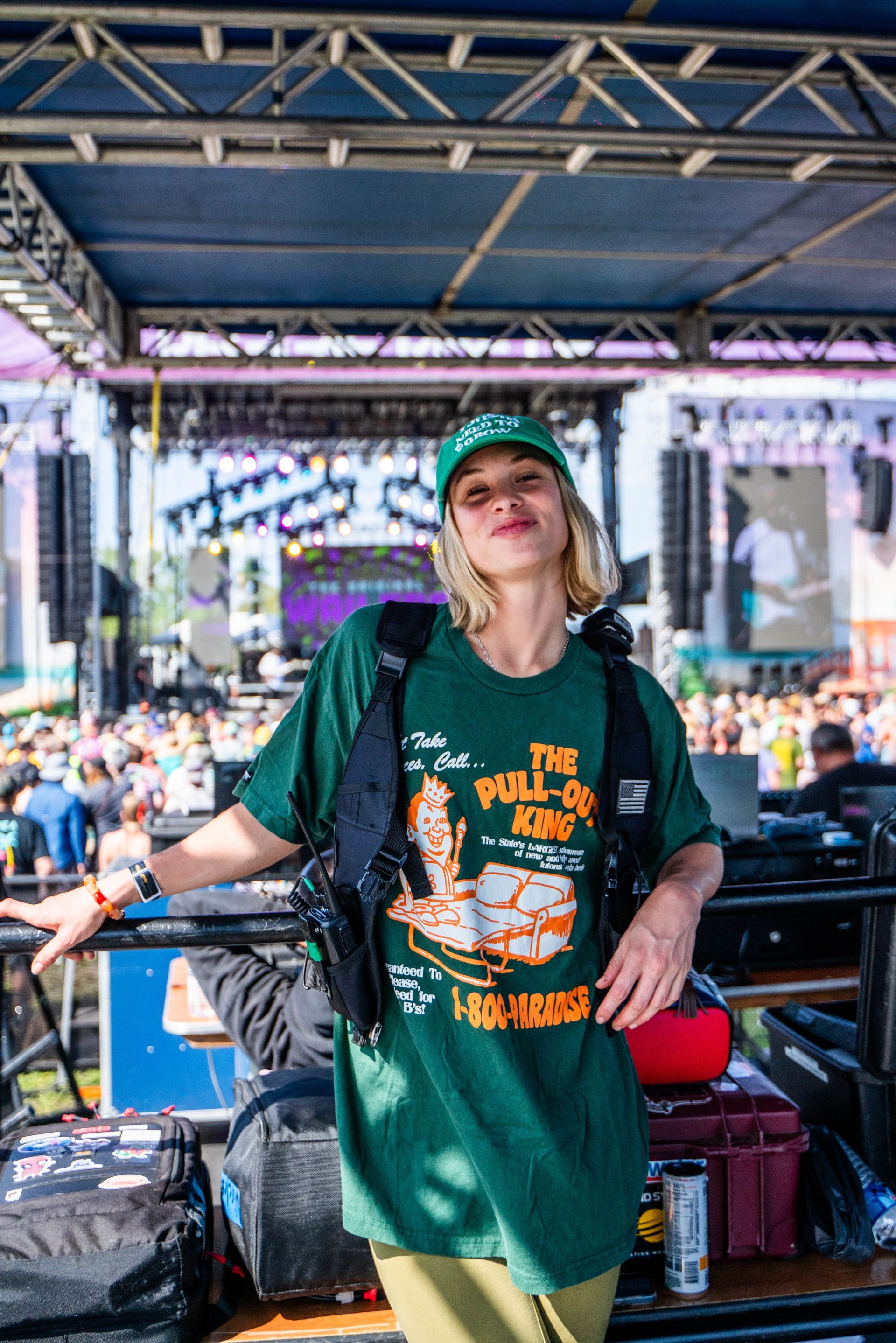 A woman in a green t-shirt and hat is standing in front of a crowd at a concert.