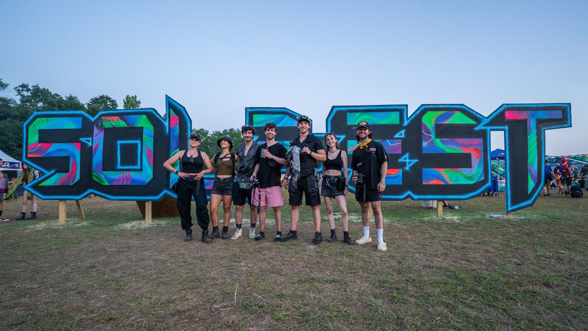 A group of people are standing in front of a sign that says solfest.