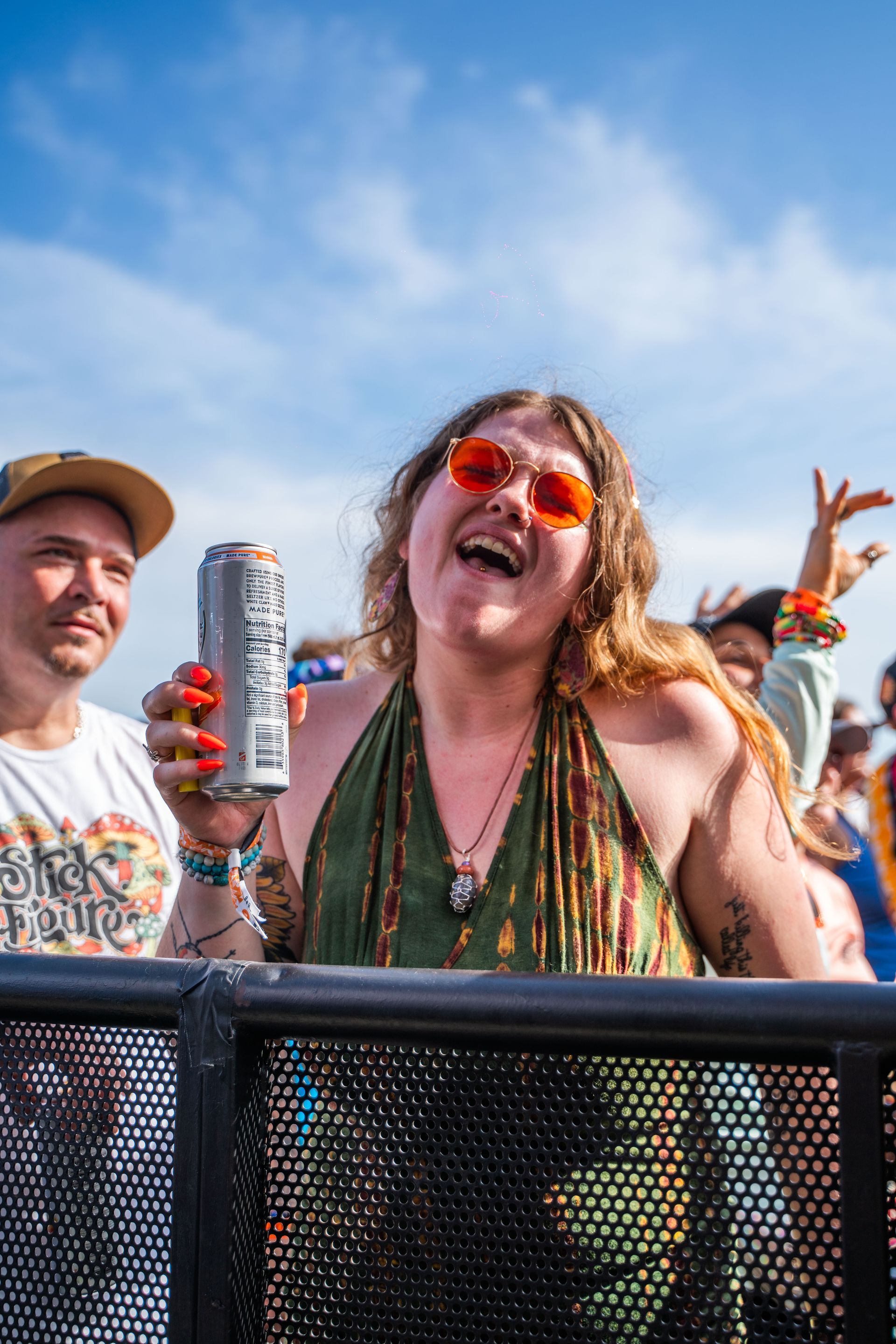 A woman is holding a can of soda and laughing at a concert.