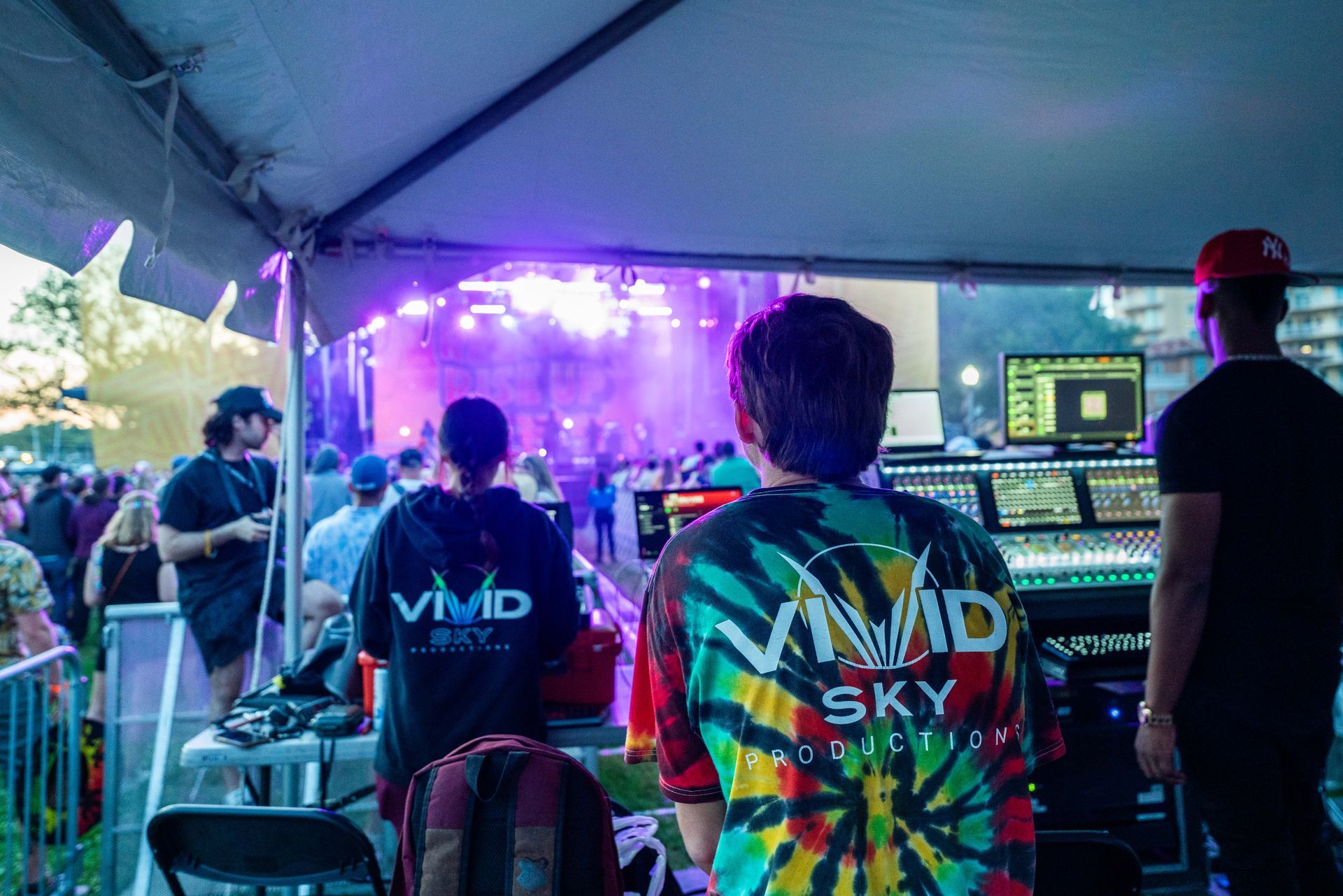 A man in a tie dye shirt is standing in front of a stage at a concert.